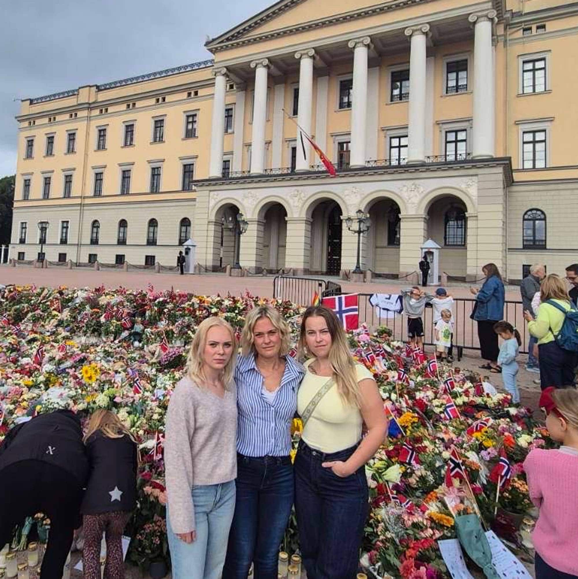 En kvinne står sammen med to jenter på slottsplassen med blomsterhavet i bakgrunnen.