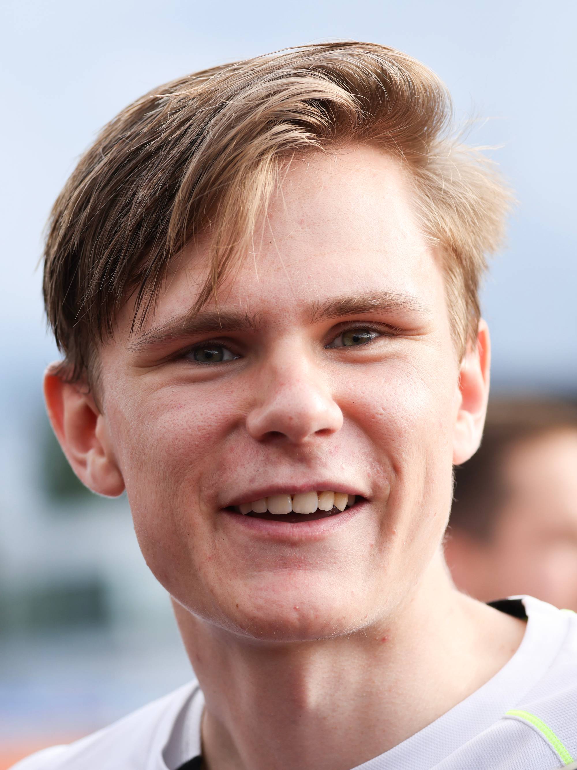Portrett av en ung mann med lyst hår som smiler. Bakgrunnen er uklar. (Bildebeskrivelsen er laget av en KI-tjeneste)