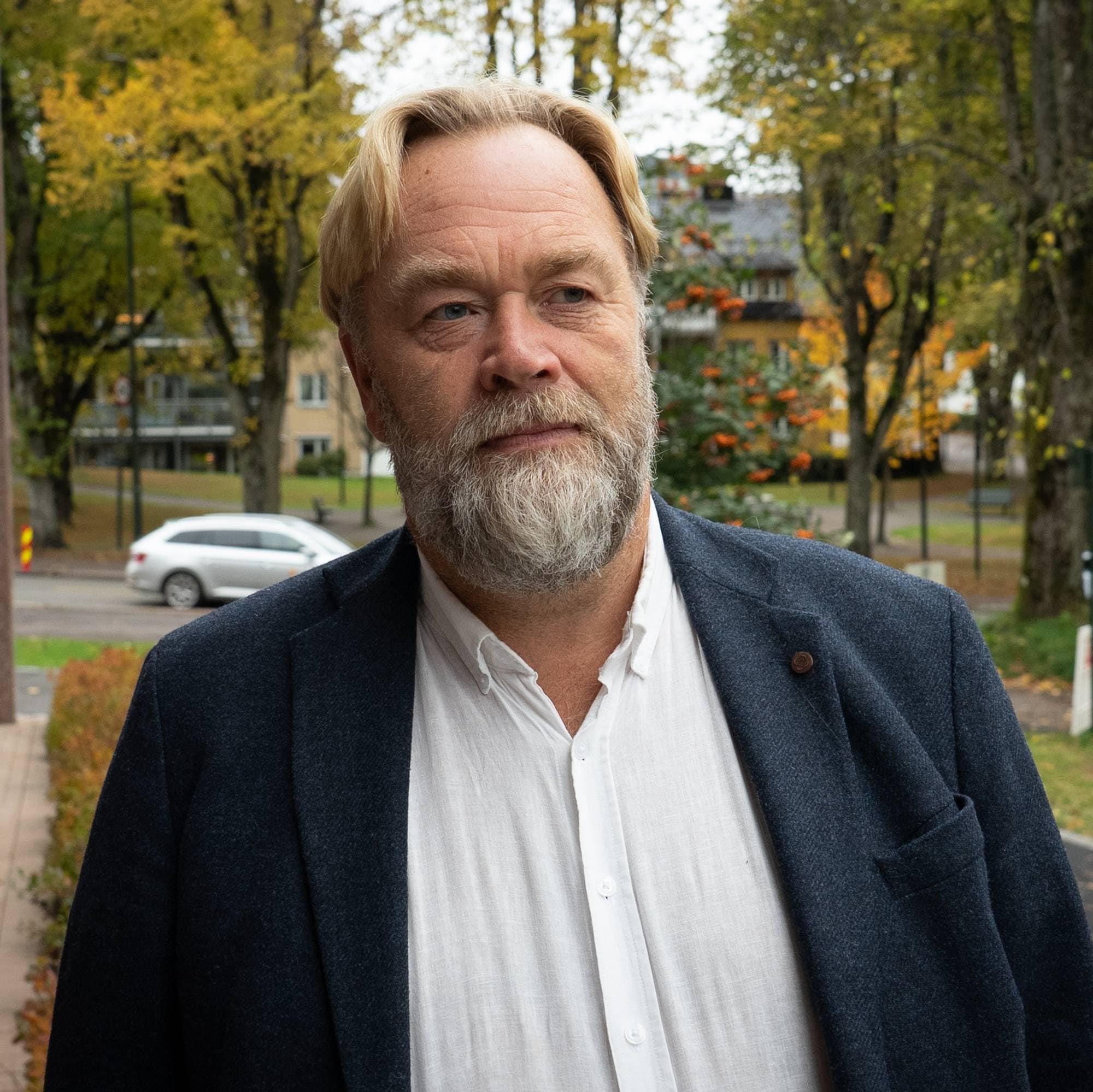 Portrettbilde av en mann som står ved siden av en bygning. I bakgrunnen ser man flere biler som kjører på en vei.