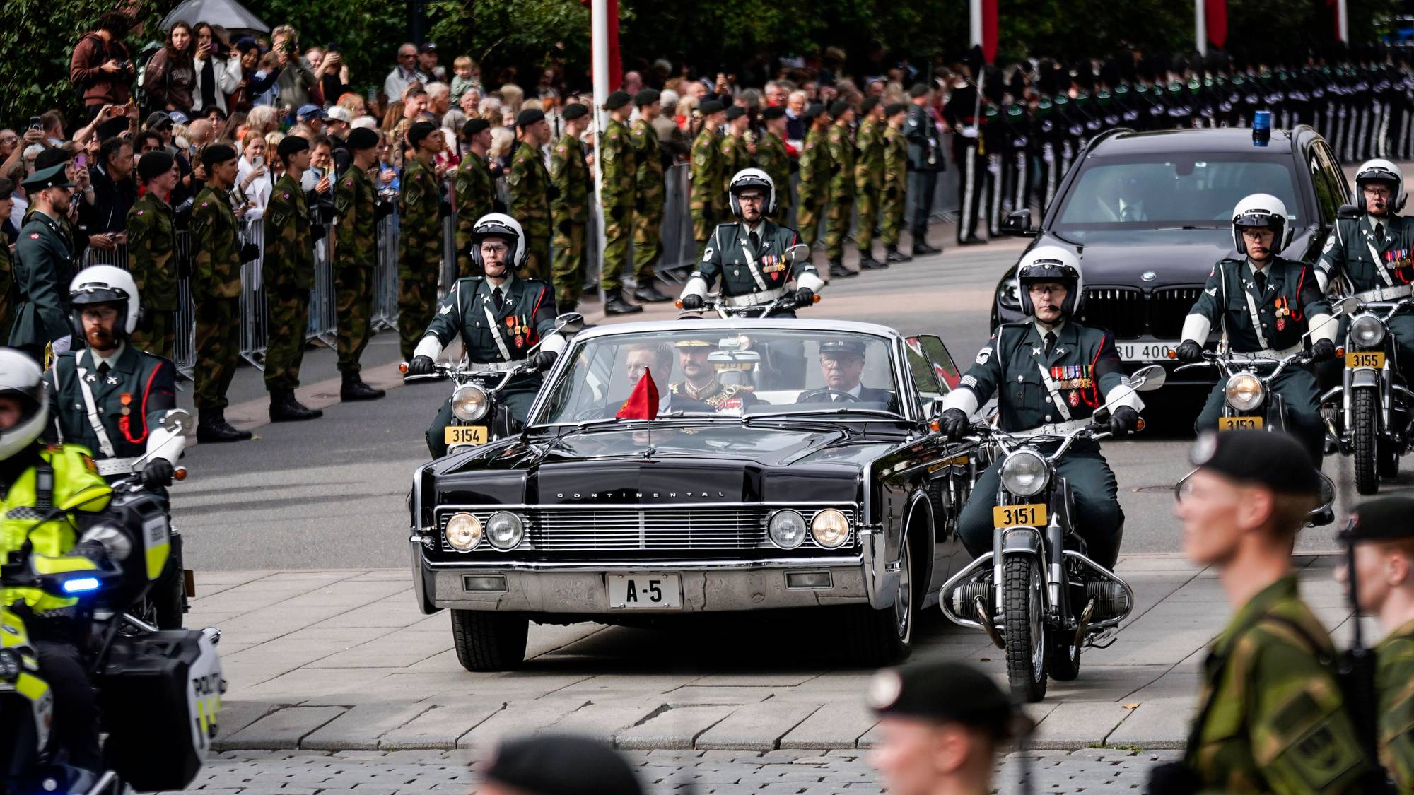 Kong Haakon kjører i åpen bil ned Karl Johan-