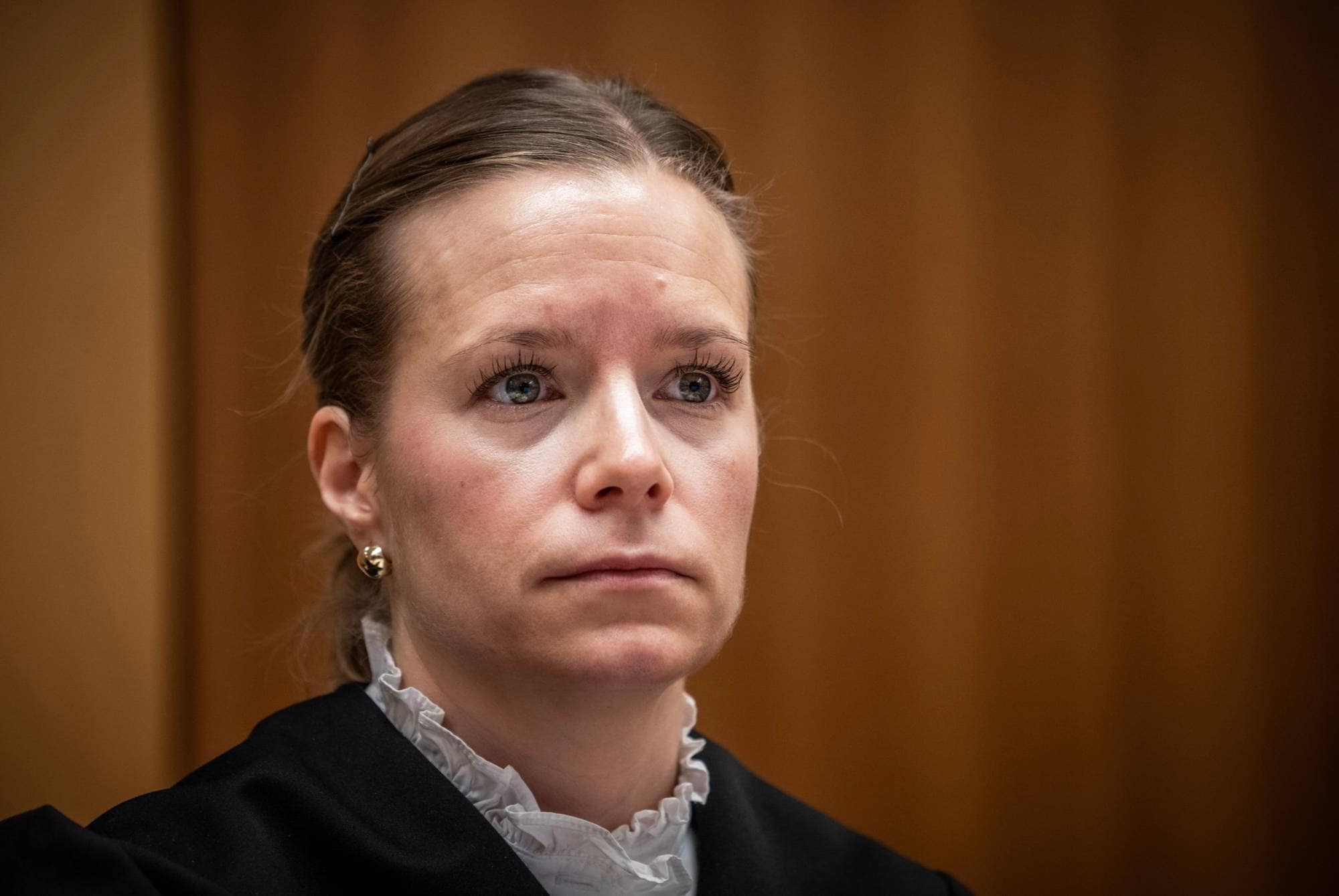 Kvinne i rettssal. Hun er iført svart embetsdrakt med hvit krage. Hun har blondt hår satt opp. Bakgrunnen er en brunmalt vegg. (Bildebeskrivelsen er laget av en KI-tjeneste)