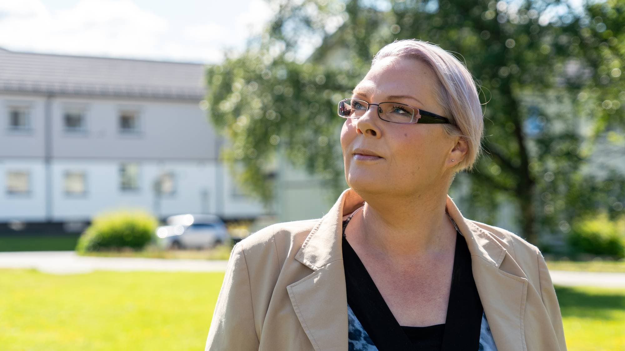 Kvinne med briller ser til siden utendørs foran en bygning