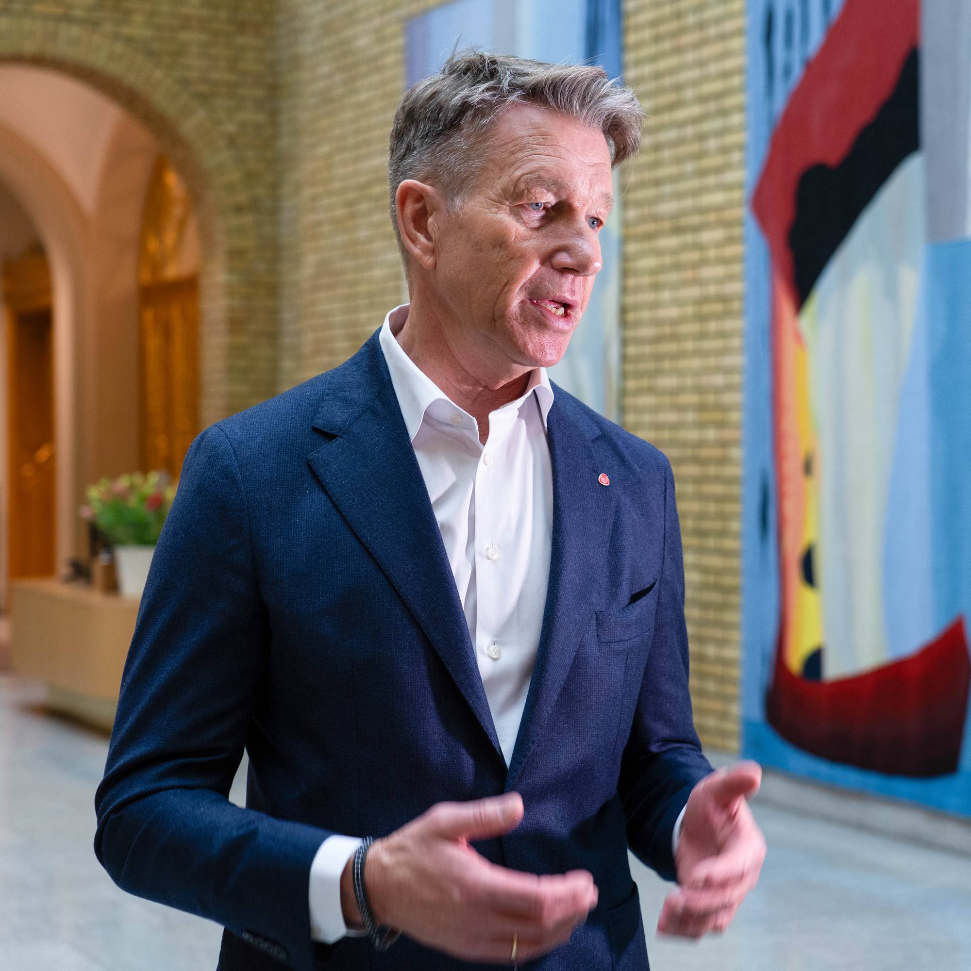 Mann i mørk med kort snakkes foran fargerikt kunstverk.
