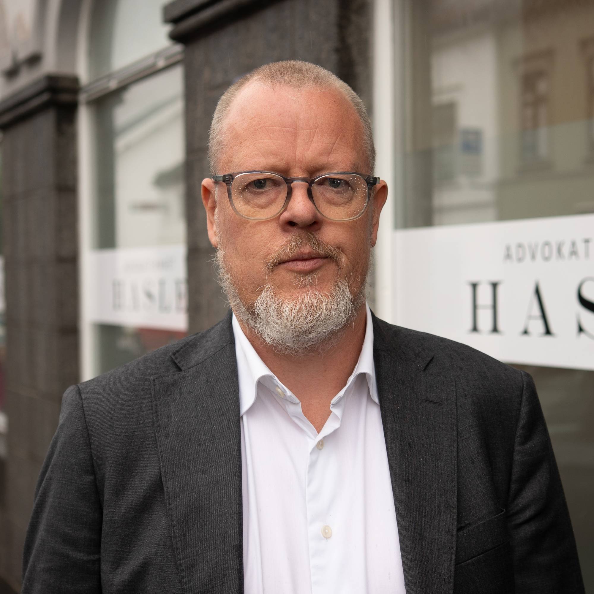 Mann med briller og skjeggestad ser mot kameraet. Han er kledd i dressjakke og hvit skjorte. 