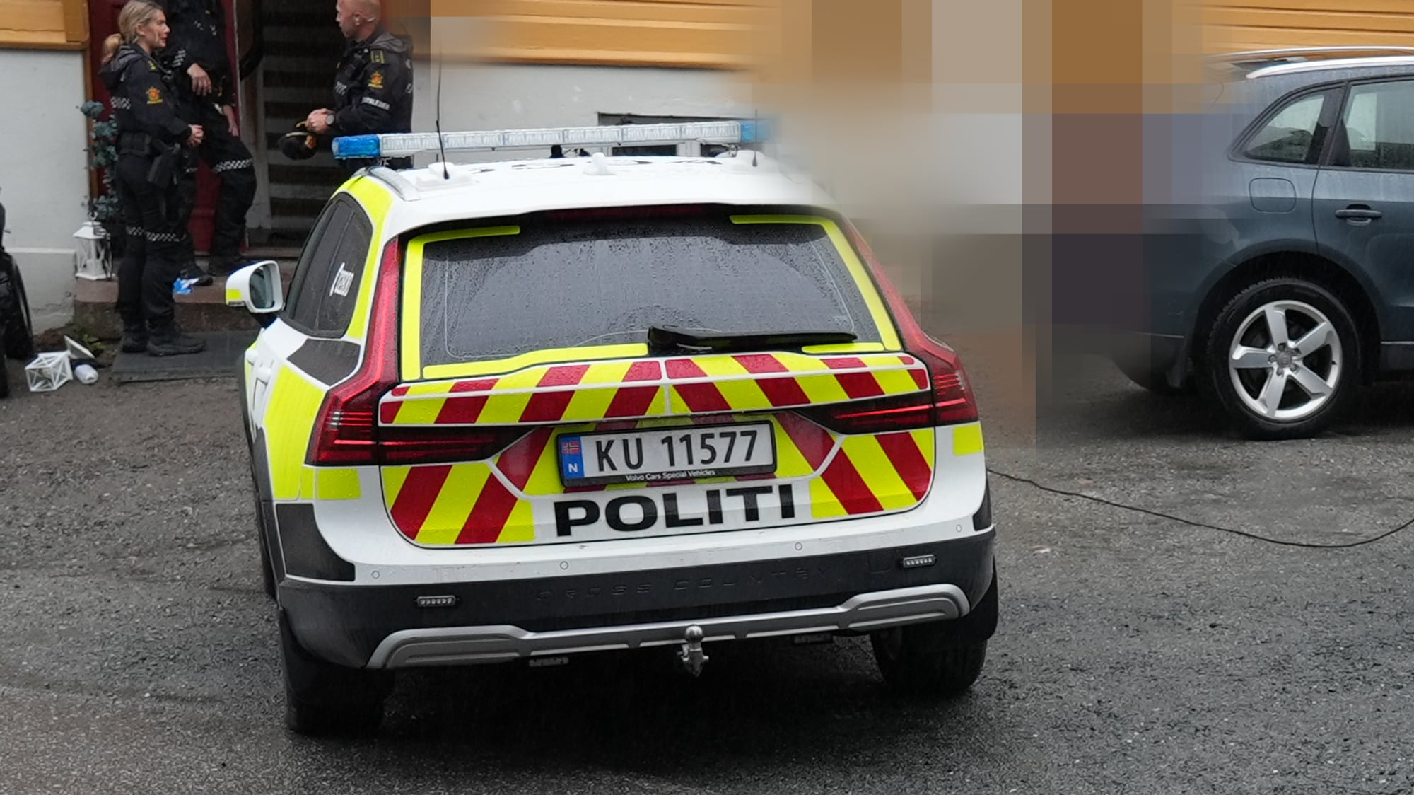 Bilde av en politibil og politifolk utenfor en bolig. Detaljer på bildet er sladdet.