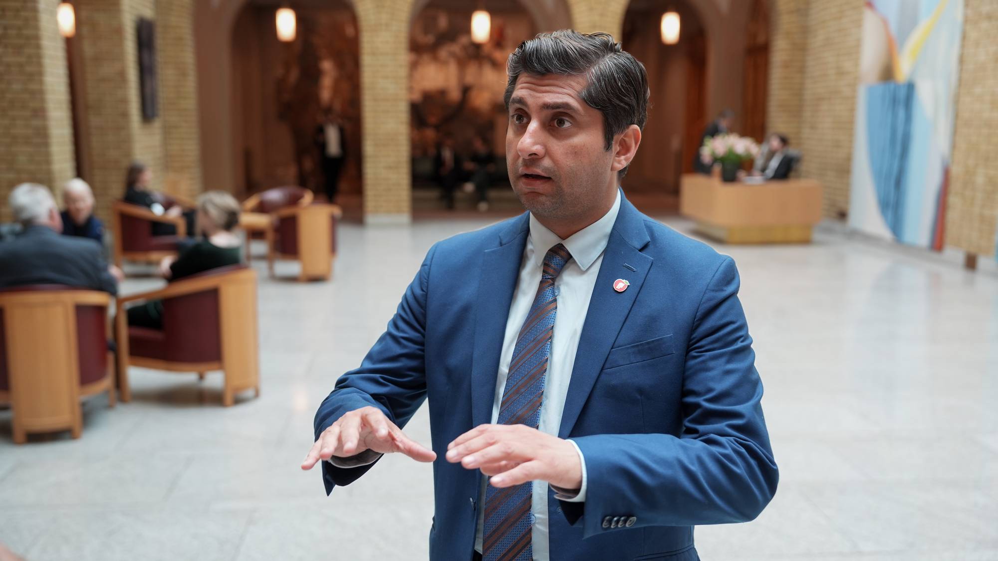 En mann snakker og bruker kroppsspråk inne i en bygning. 