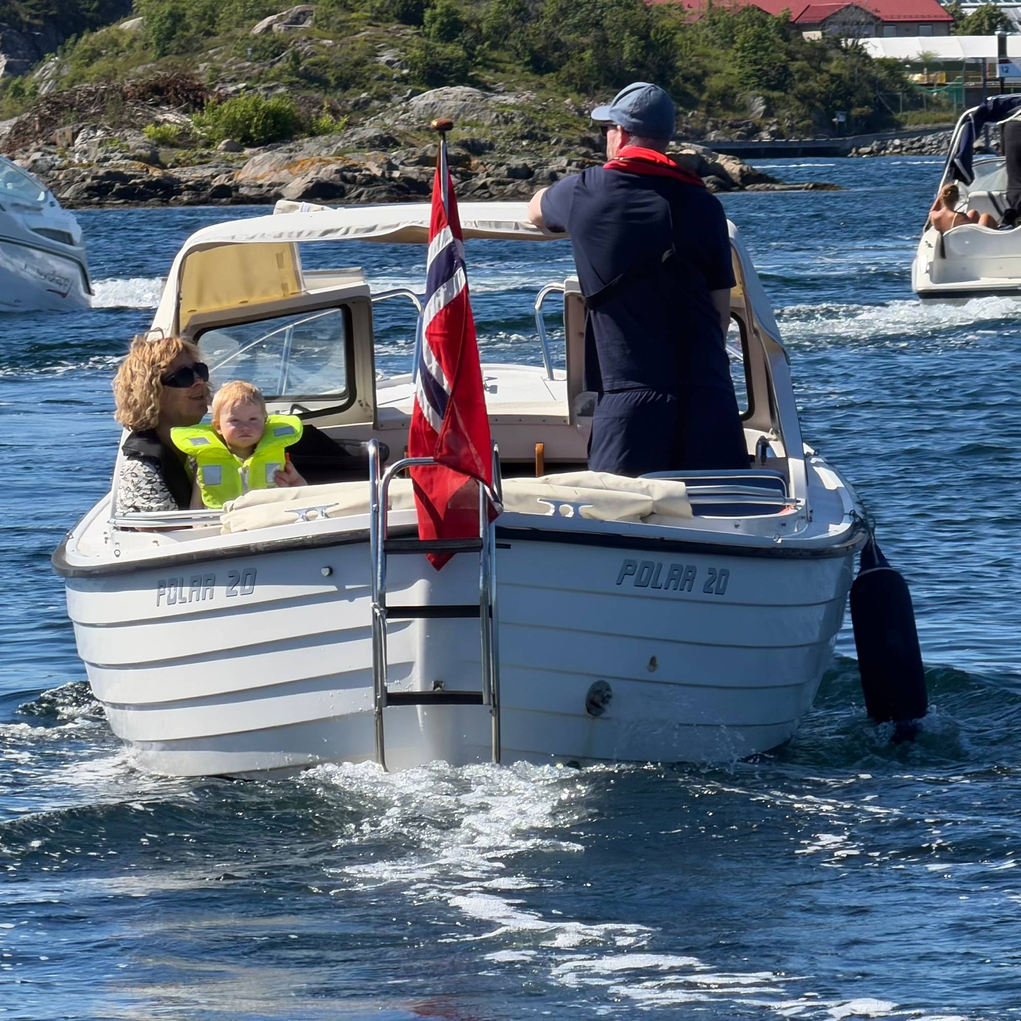 Sjekte med to personer sett bakfra. Flere båter passerer. 