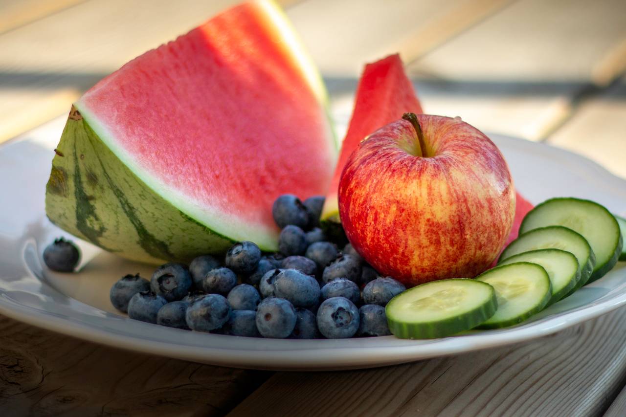 Et smakfullt fruktfat med saftige meloner, epler, agurker og blåbær. Du får vann i munnen av å se på bildet.