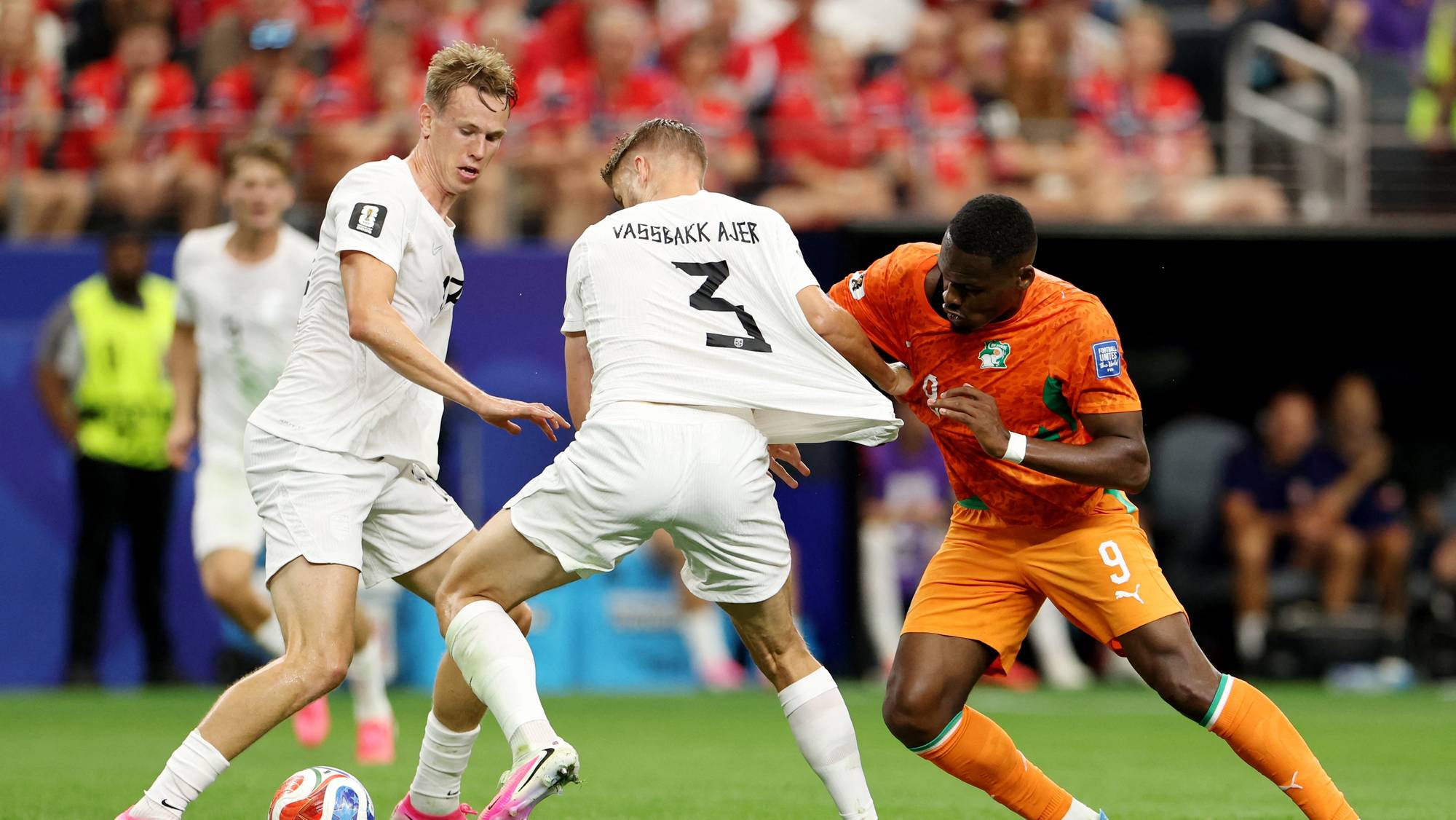 Norsk fotballspiller i hvit drakt holder i trøya til en motspiller i oransje drakt under en kamp. (Bildebeskrivelsen er laget av en KI-tjeneste)