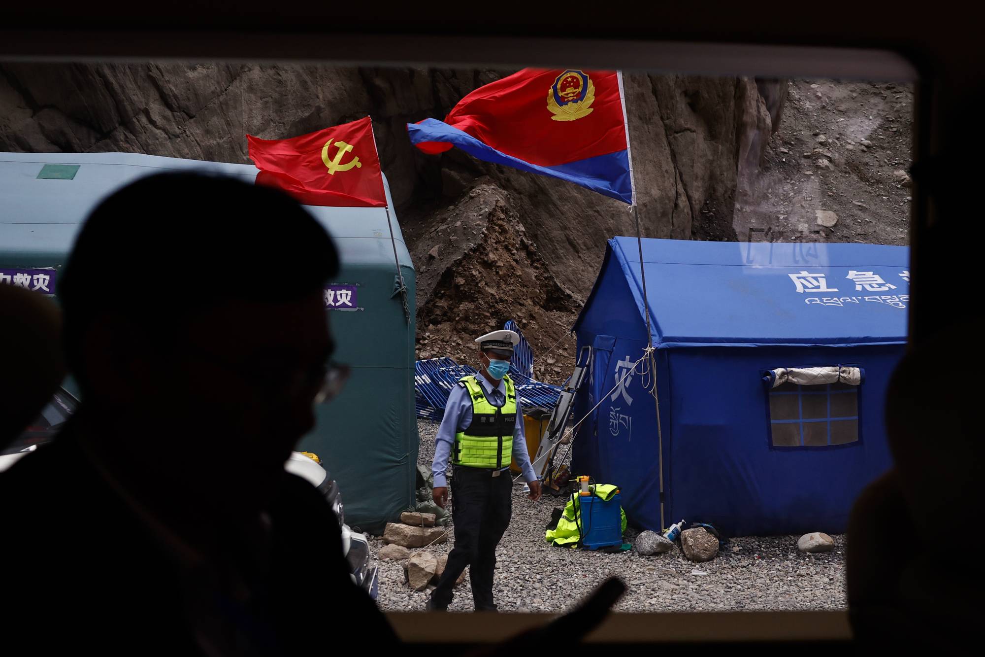 En politimann står ved telt i området der grensestasjonen i Gyirong var før den ble vasket bort av flommen. 