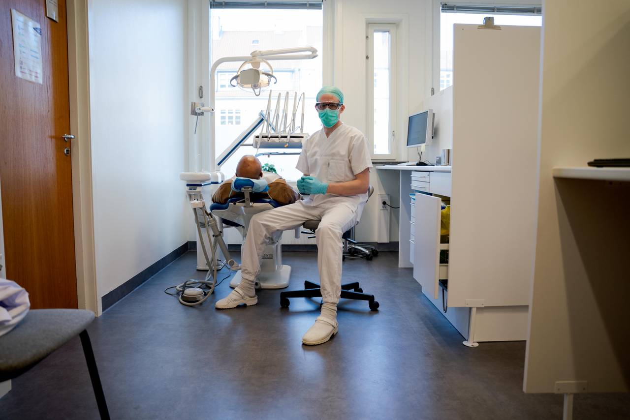 Andreas sitter ved siden av tannlegestolen, hvor en pasient er til behandling.