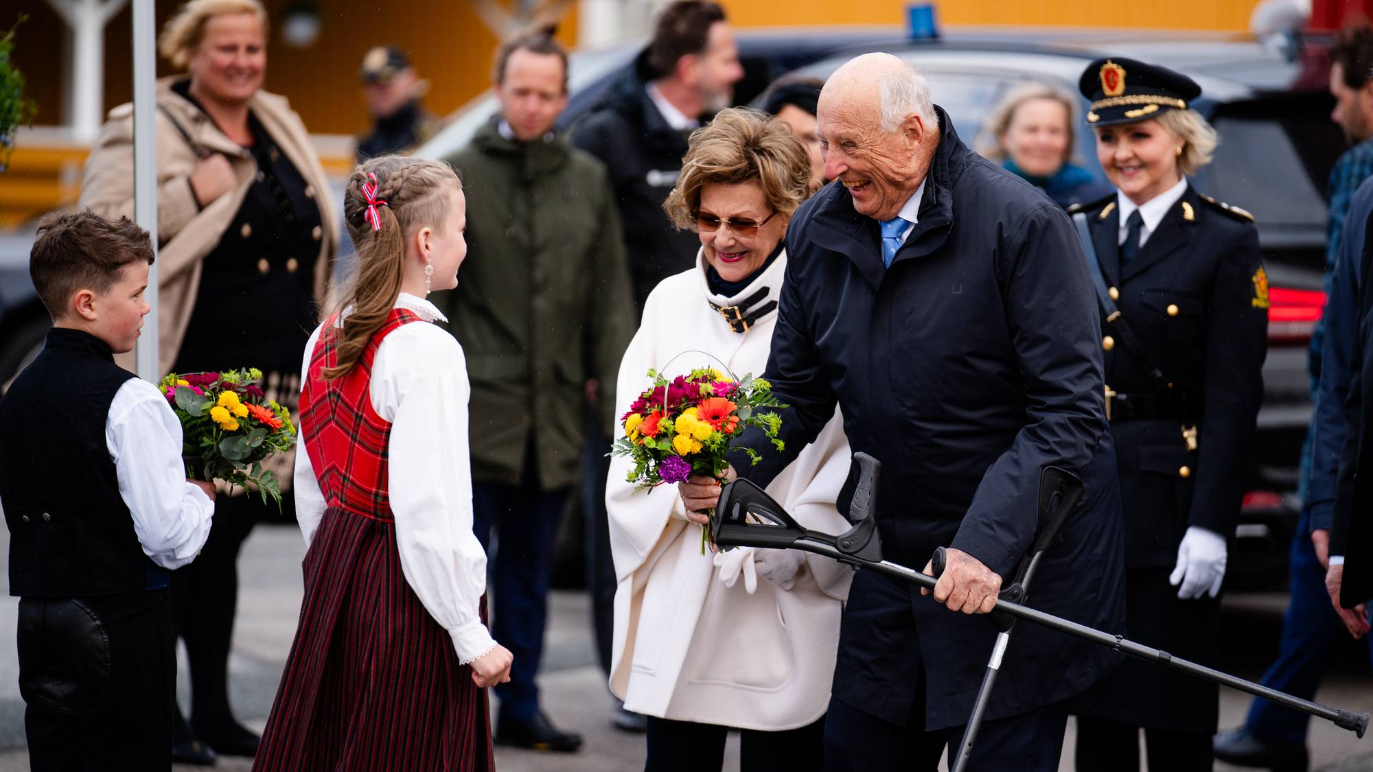 Kong Harald og dronning Sonja får blomster av blomsterbarn når de kommer i land i Hemnesberget under fylkesturen i Nordland i juni 2023