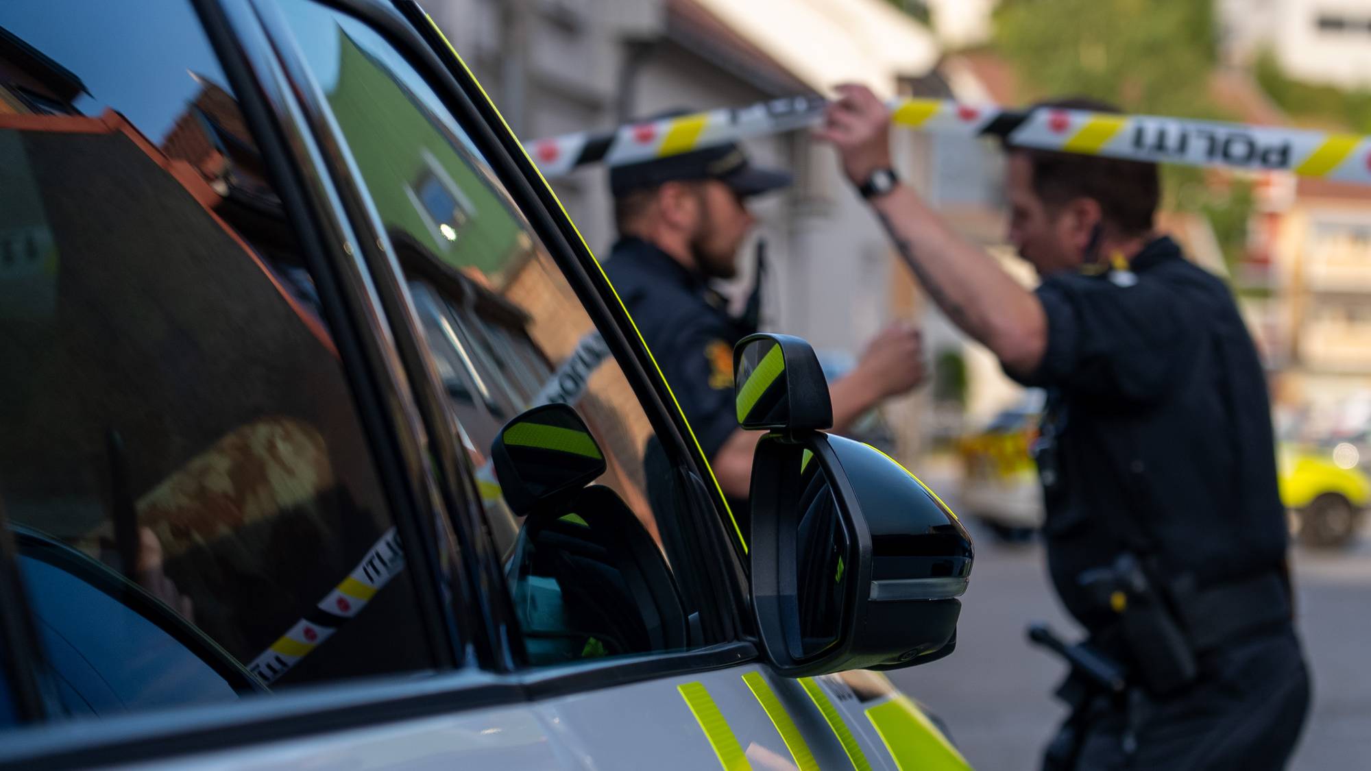 Politi ved en avsperret gate. Politibil i forgrunnen og politibetjenter i bakgrunnen. (Bildebeskrivelsen er laget av en KI-tjeneste)