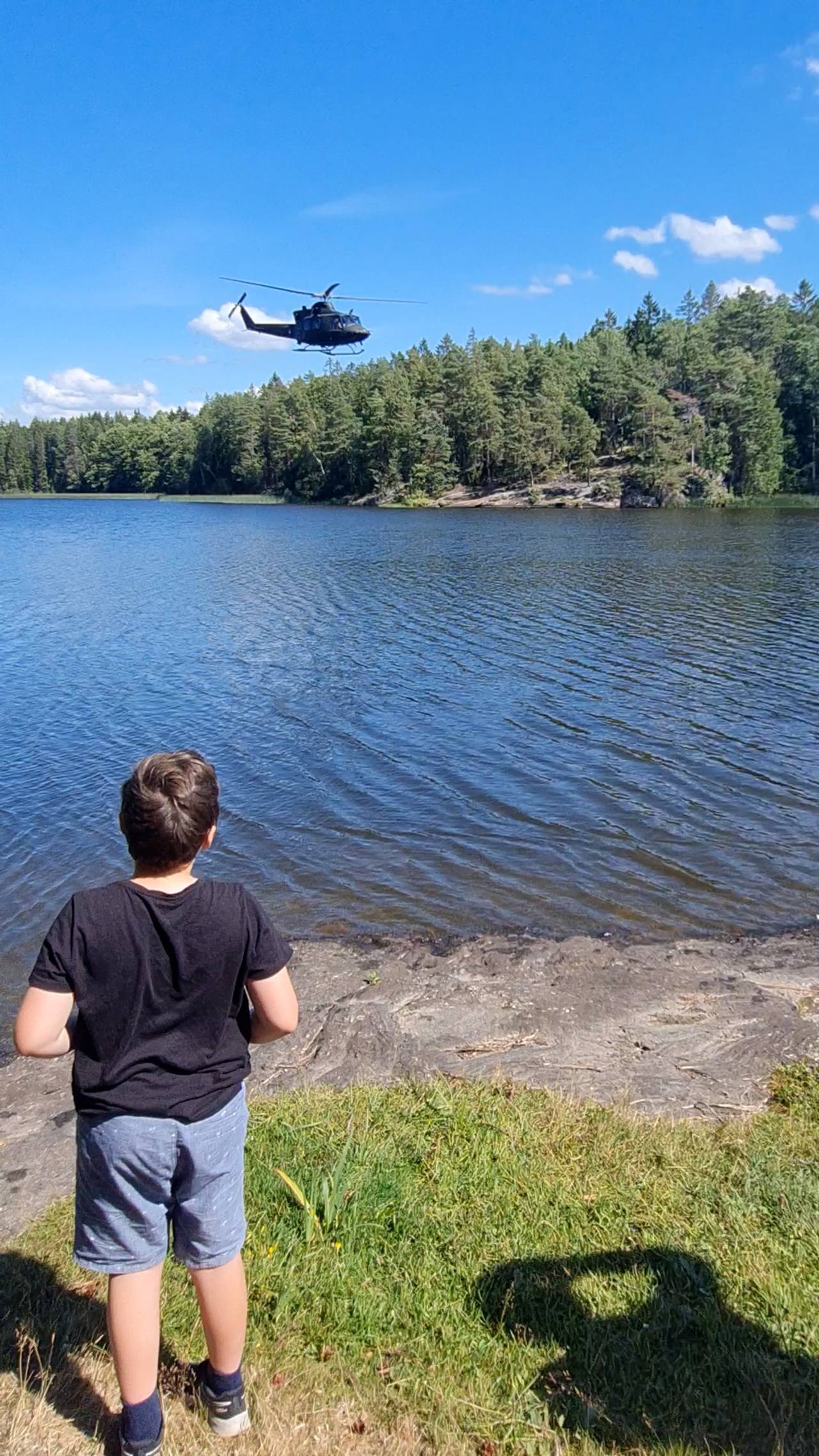 En liten gutt ser på et helikopter som flyr lavt over Vansjø.