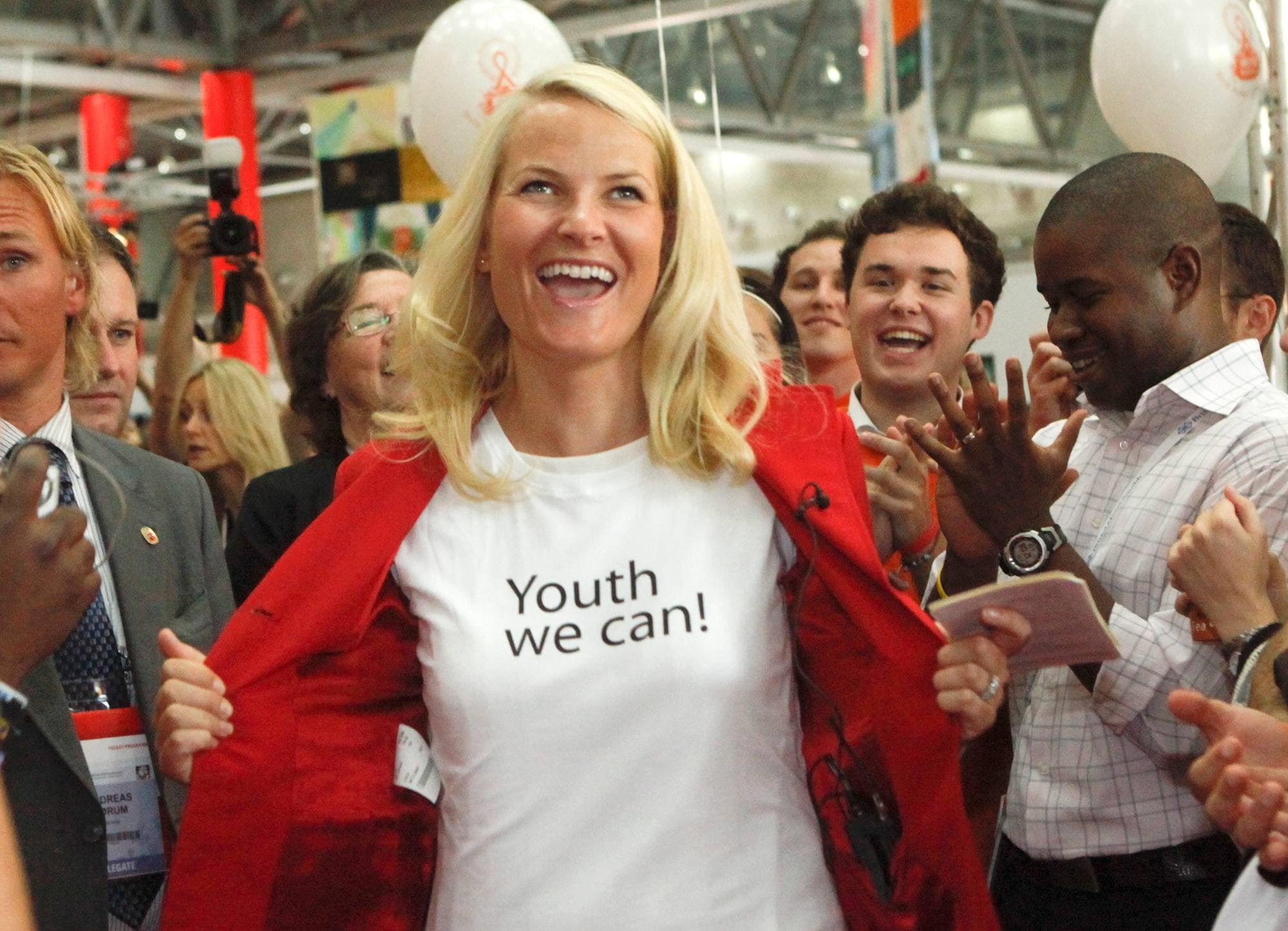 Kronprinsesse Mette-Marit åpner jakken sin og viser frem påskriften på t-skjorten, der det står "Youth we can!", på Den internasjonale aids-konferansen i Wien i 2010