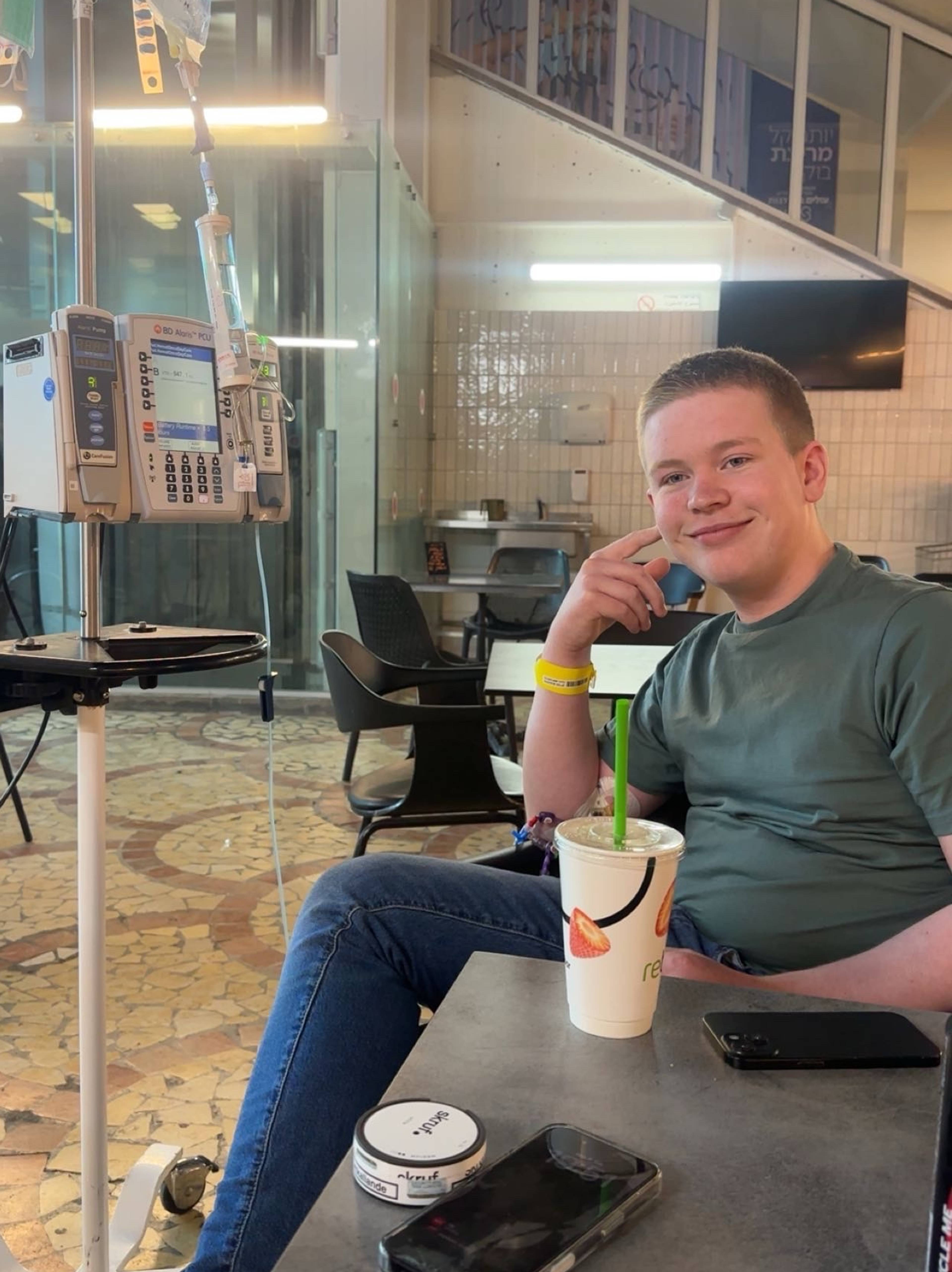 Ein ung mann smiler til kameraet med eit infusjonsstativ ved sidan av seg.
