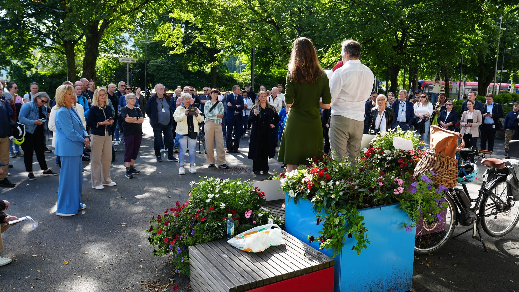 En kvinne og en mann snakker til en folkemengde i en park. 