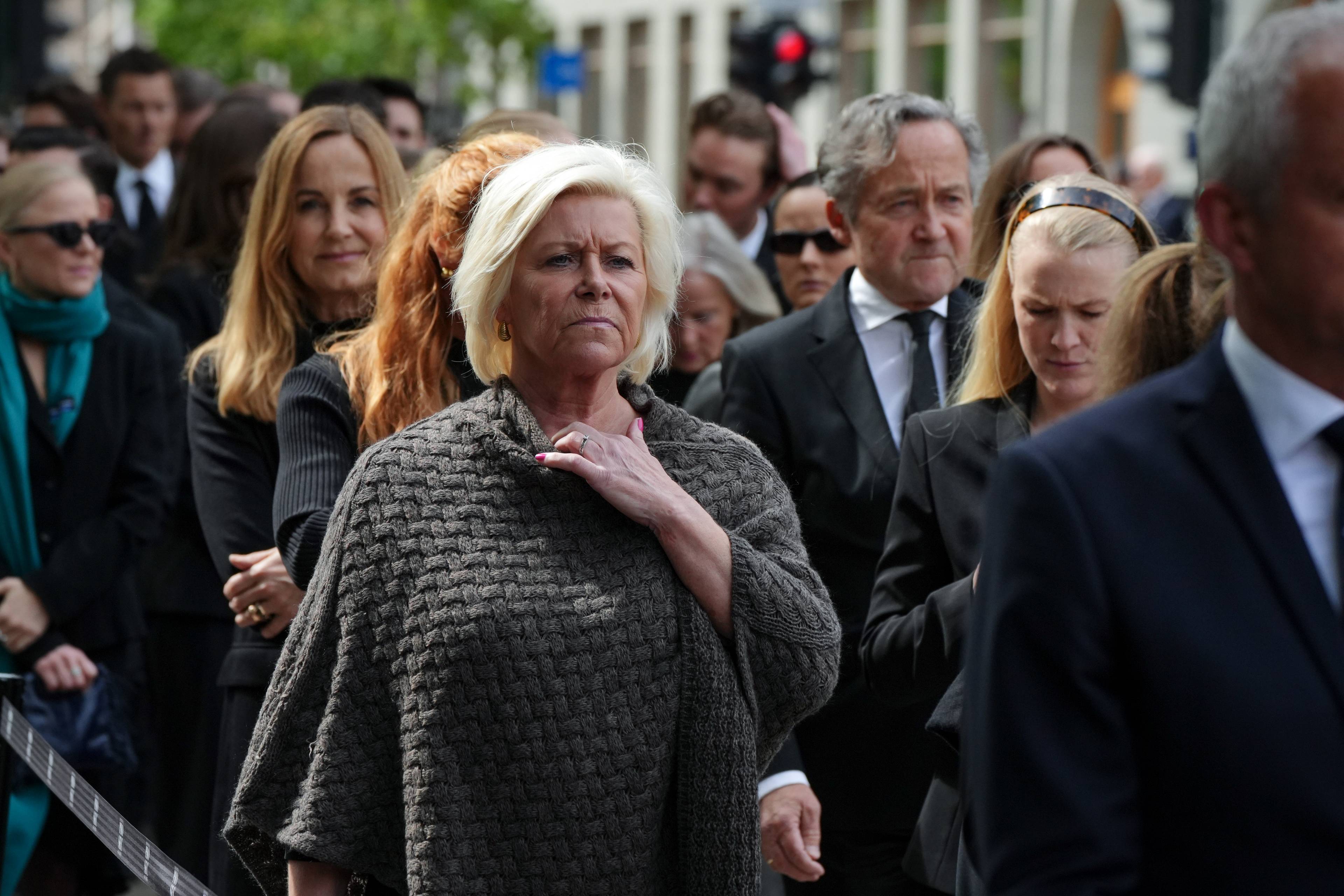 Siv Jensen står i kø utenfor Oslo Domkirke. Det er mange andre mennesker rundt henne. Hun har kvitt hår og har på seg en grå strikket poncho.