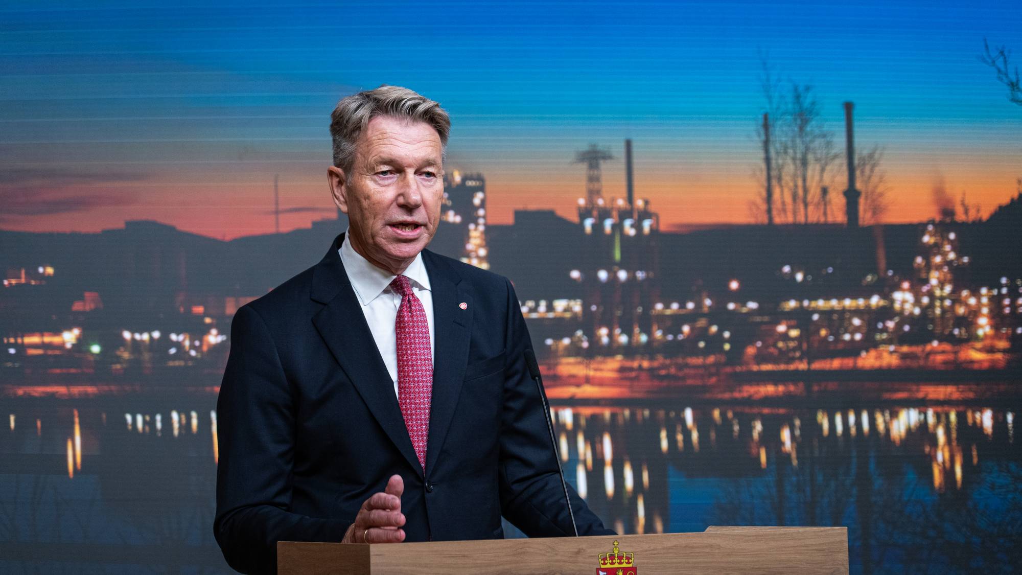 Energiminister Terje Aasland taler fra en talerstol foran en skjerm med industrimotiv. (Bildebeskrivelsen er laget av en KI-tjeneste)