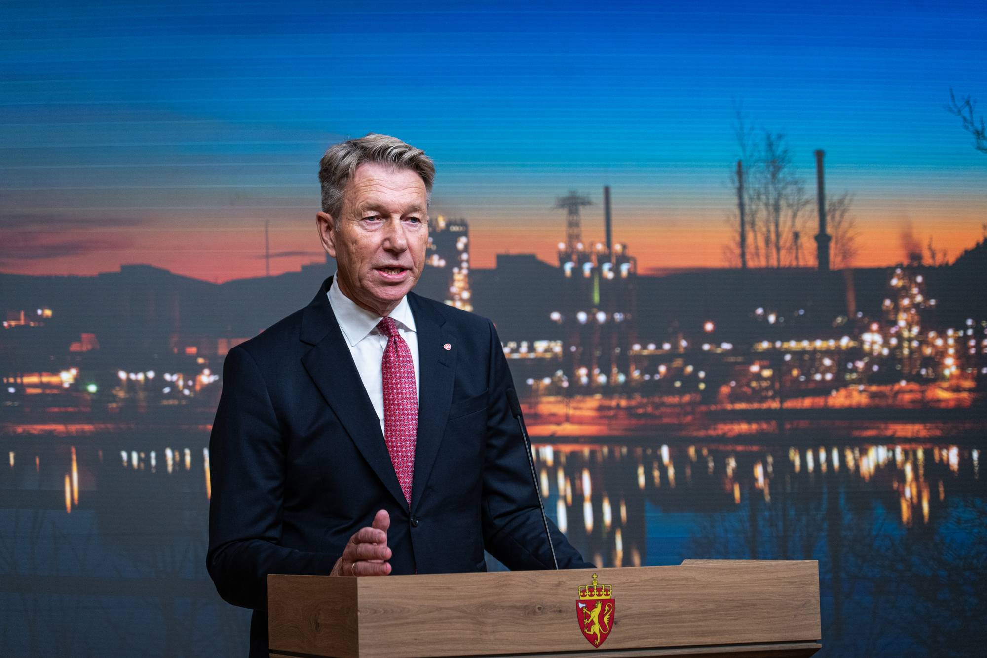 Energiminister Terje Aasland taler fra en talerstol foran en skjerm med industrimotiv.