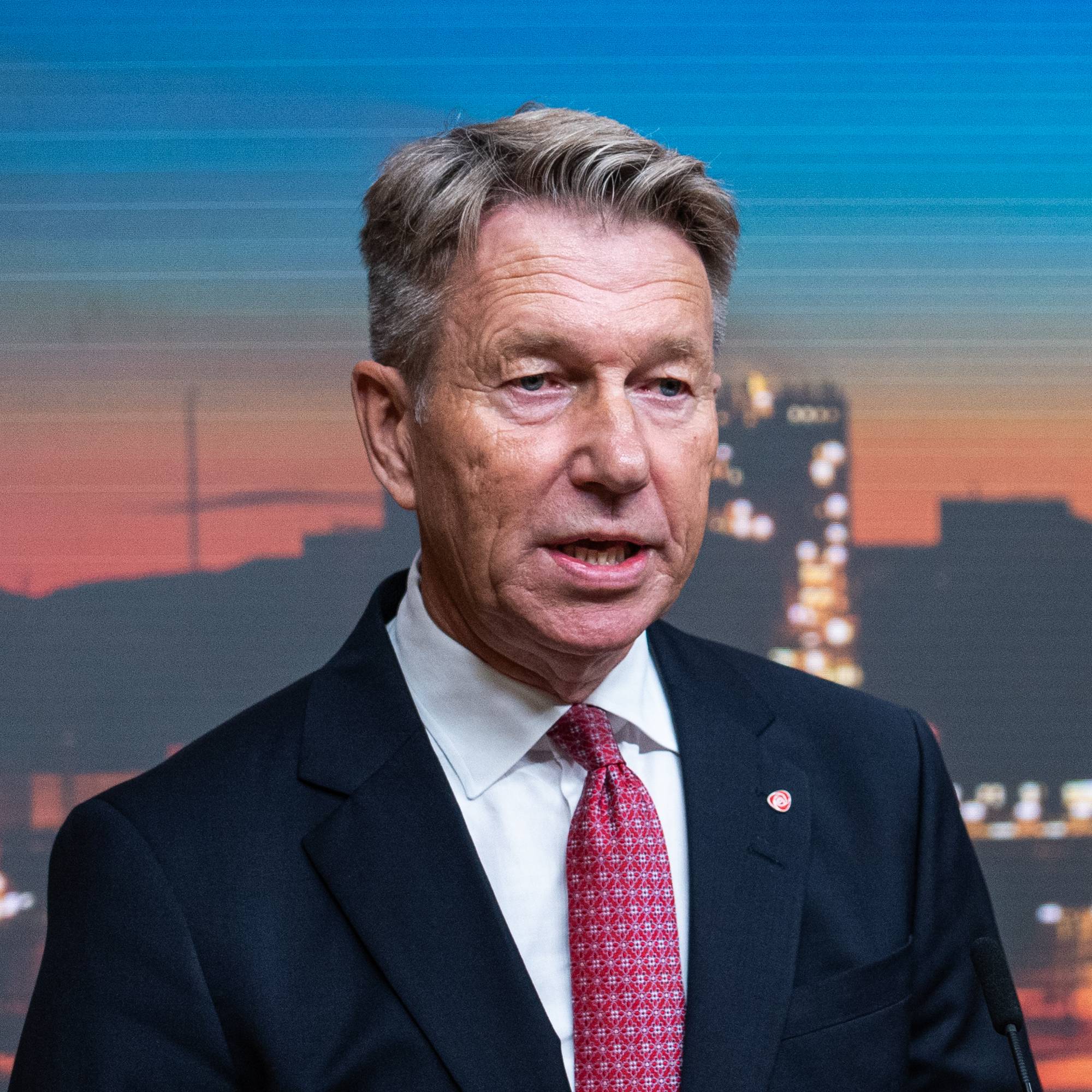 Energiminister Terje Aasland taler fra en talerstol foran en skjerm med industrimotiv. (Bildebeskrivelsen er laget av en KI-tjeneste)