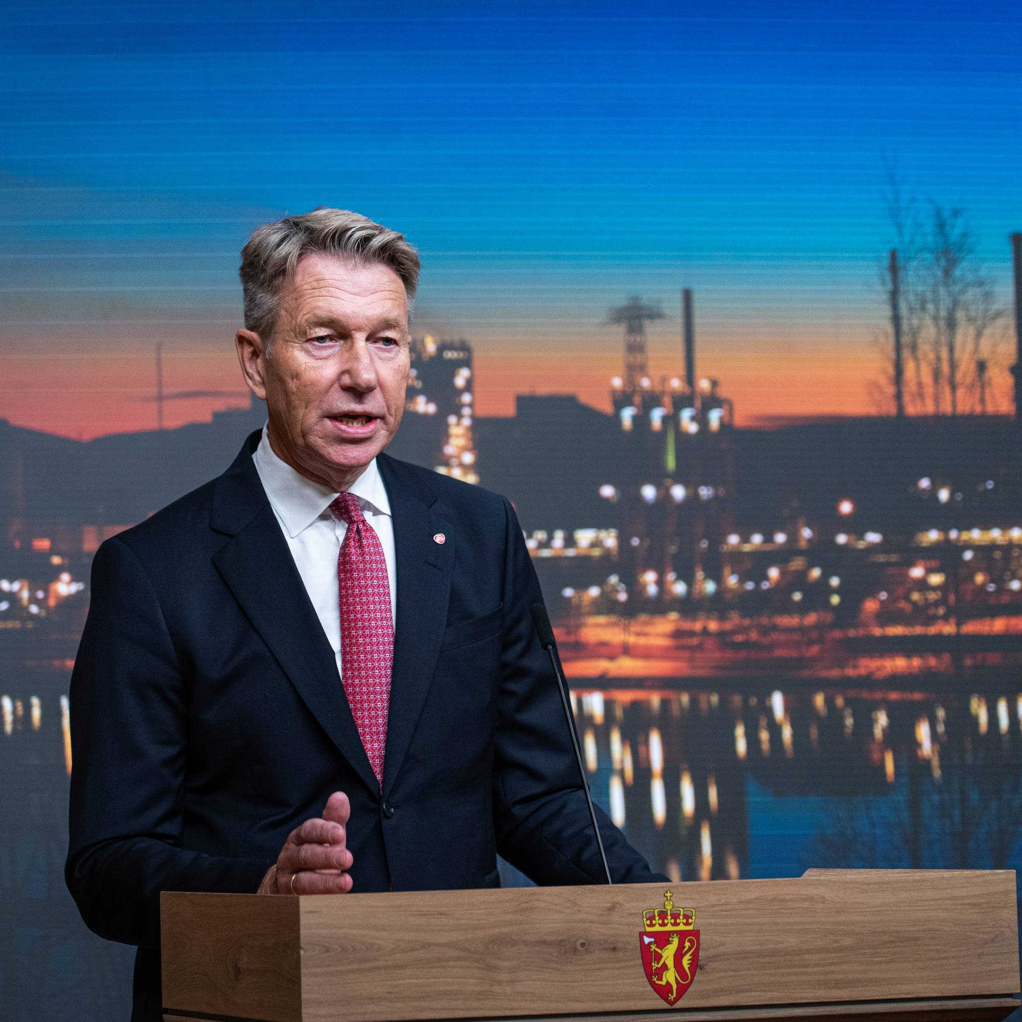 Energiminister Terje Aasland taler fra en talerstol foran en skjerm med industrimotiv.