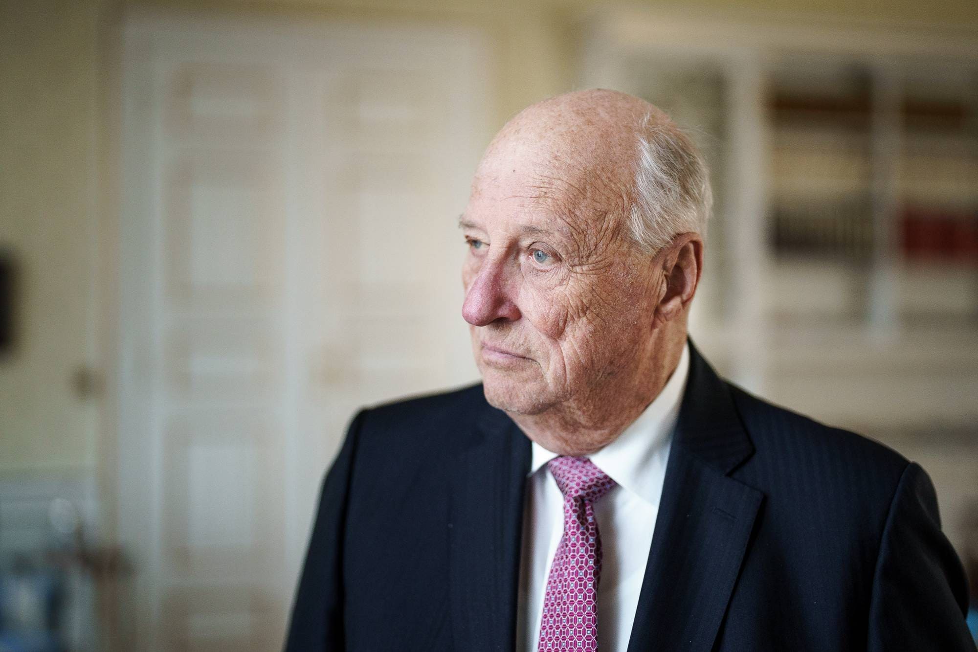 Kong Harald står på kontoret sitt på Slottet og ser ut av vinduet
