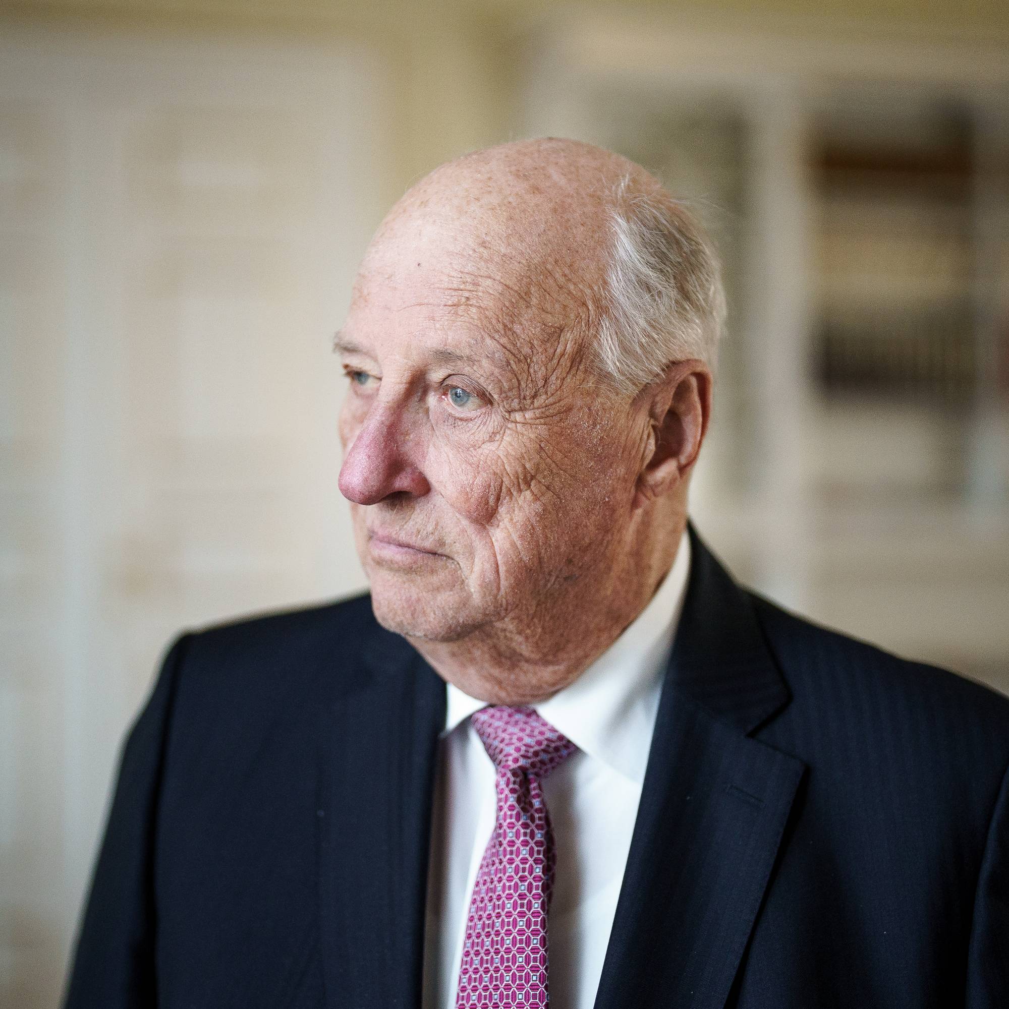 Kong Harald står på kontoret sitt på Slottet og ser ut av vinduet