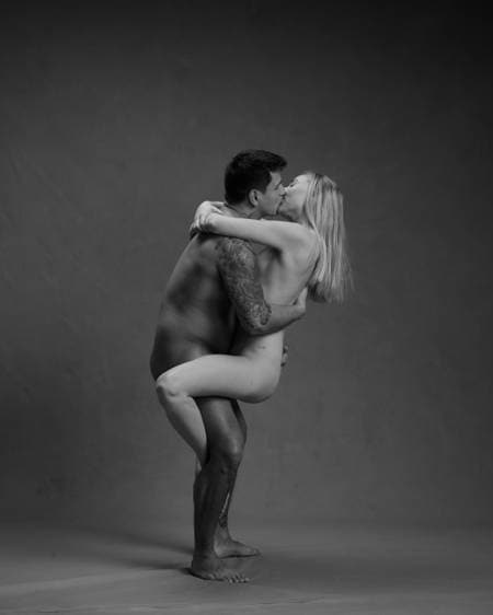 En naken mann står på gulvet og løfter en naken kvinne mens de kysser
