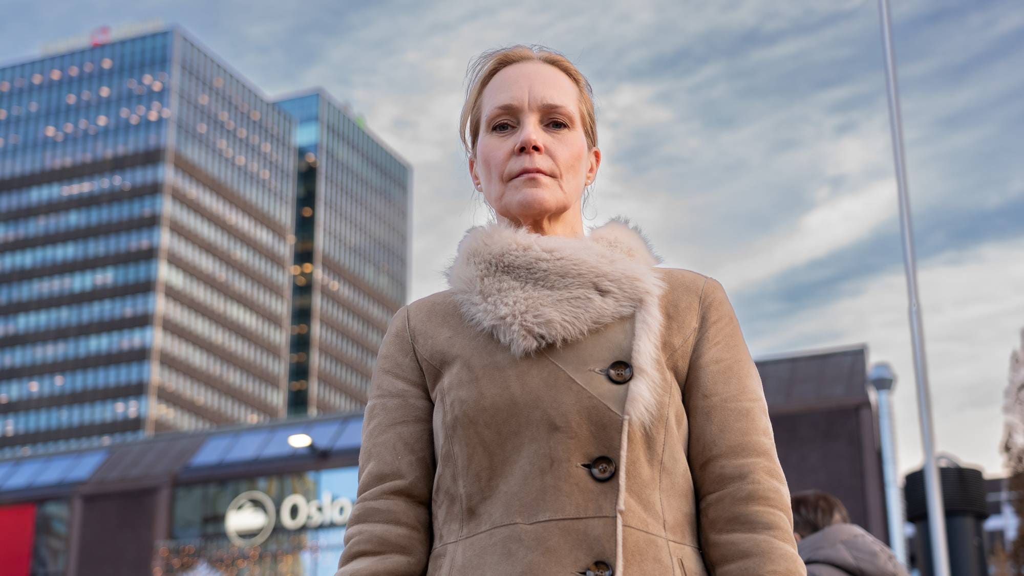 Hanna Geiran sett i froskeperspektiv i bybildet. Hun har oppsatt hår og en frakk med pelskrage. 