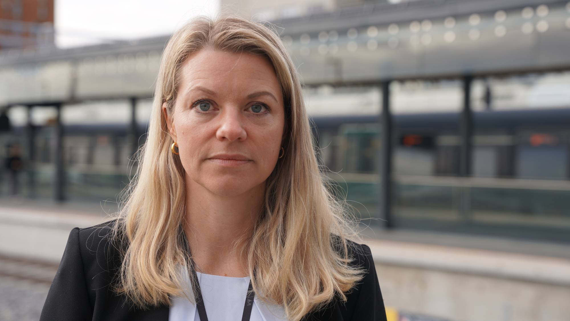 en kvinne med blondt hår står på perrongen på en stasjon