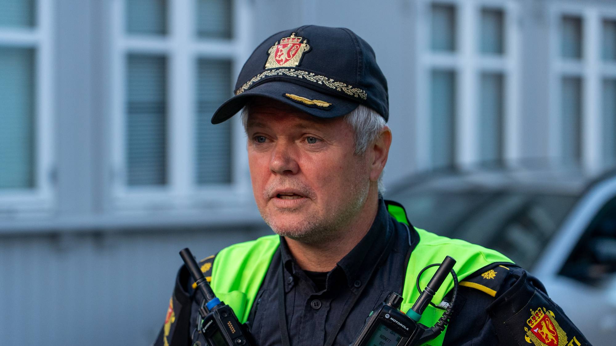 En politibetjent i uniform med gul refleksvest og politilue snakker til kameraet. (Bildebeskrivelsen er laget av en KI-tjeneste)