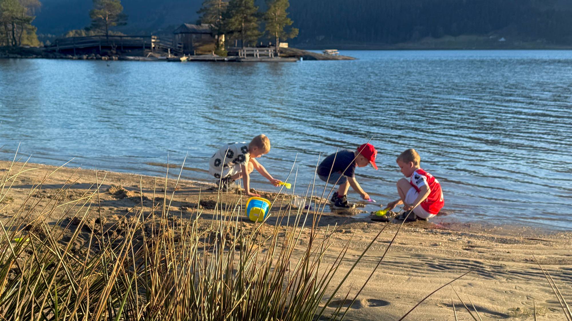 Tre barn leker med bøtte og spader på en sandstrand. 