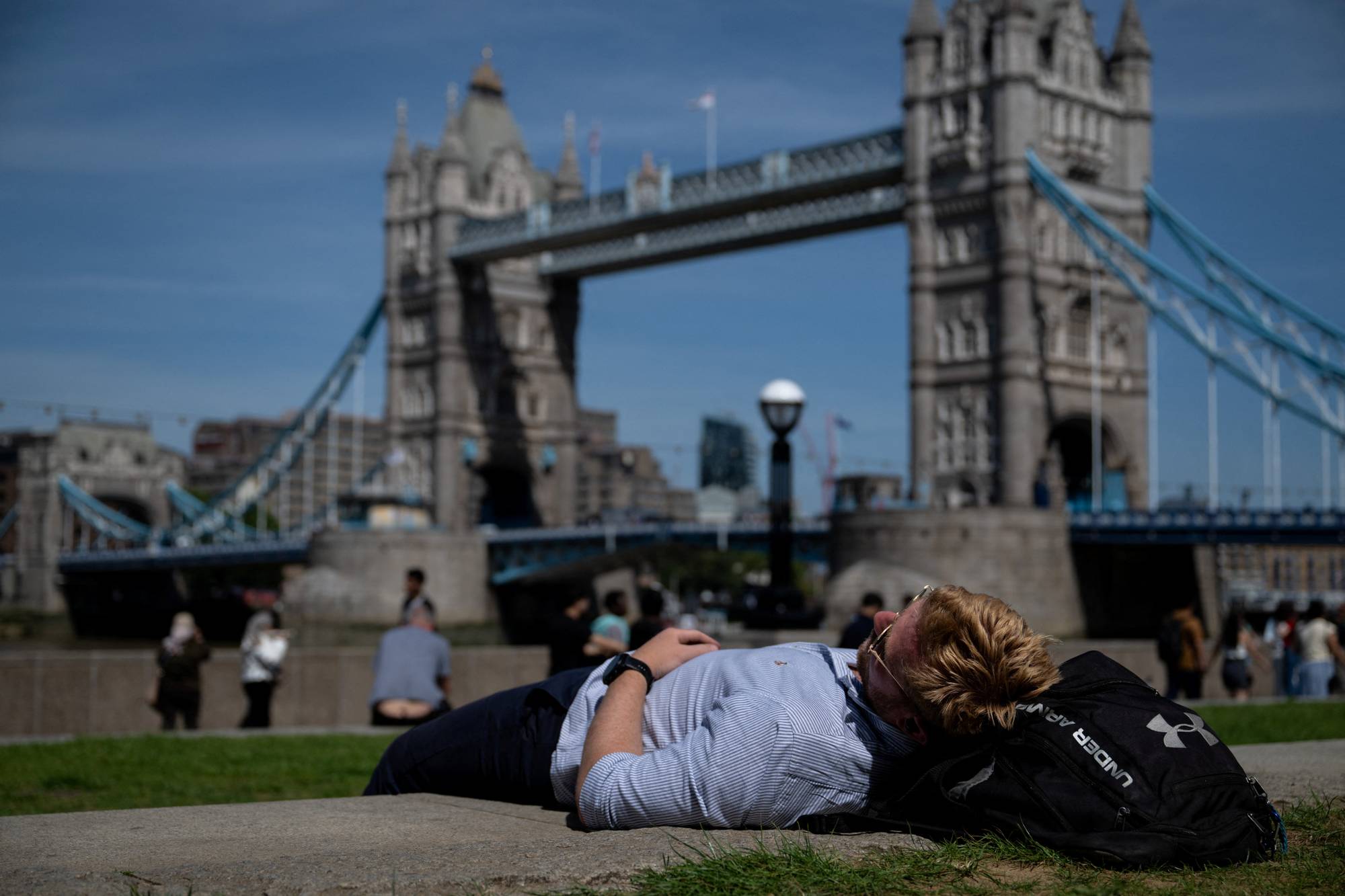En mann ligger i sola ved Tower Bridge