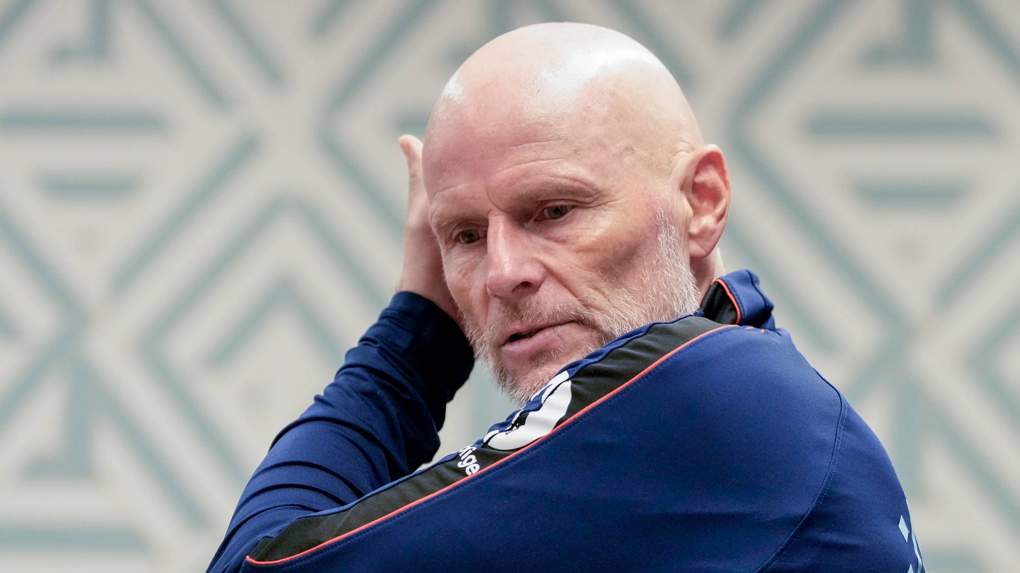 Ståle Solbakken i blå treningsgrenser ser til siden med hånden bak hodet. (Bildebeskrivelsen er laget av en KI-tjeneste)