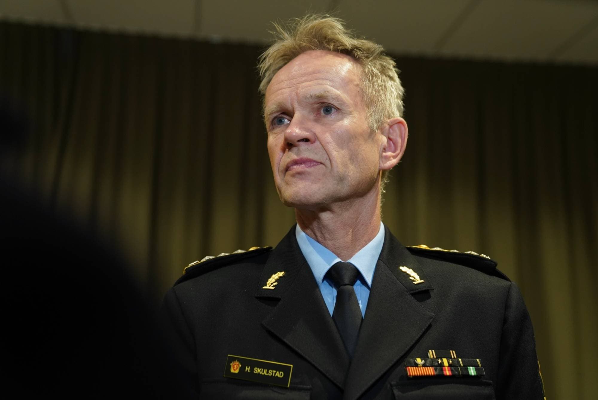 En mann i uniform, iført skjorte og slips. Han har en plakett med navnet H. Skulstad på brystet.