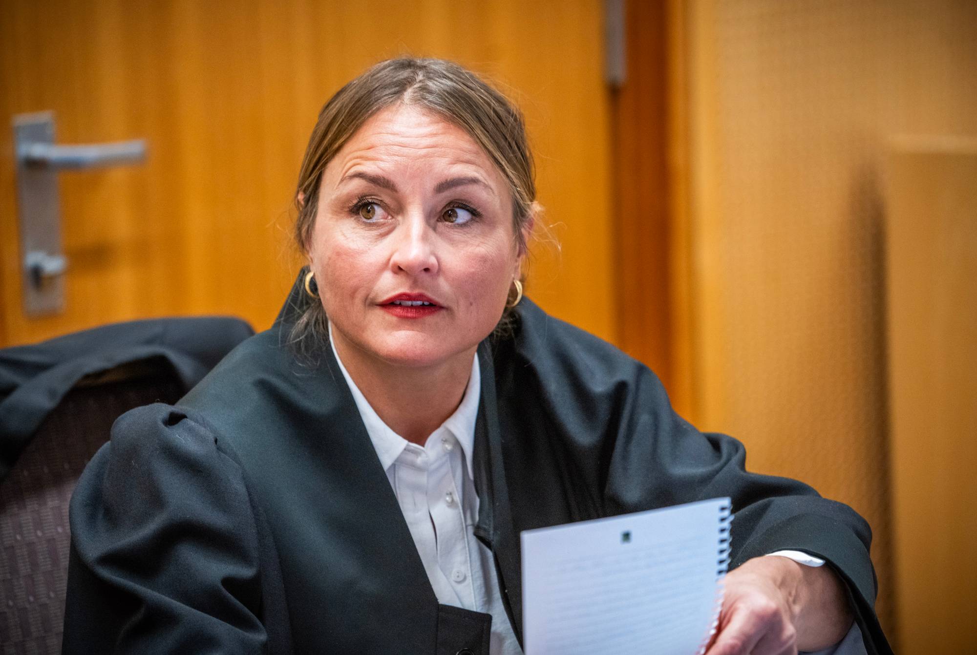 Kvinne i svart advokatkappe sitter med et notat i en rettssal. 