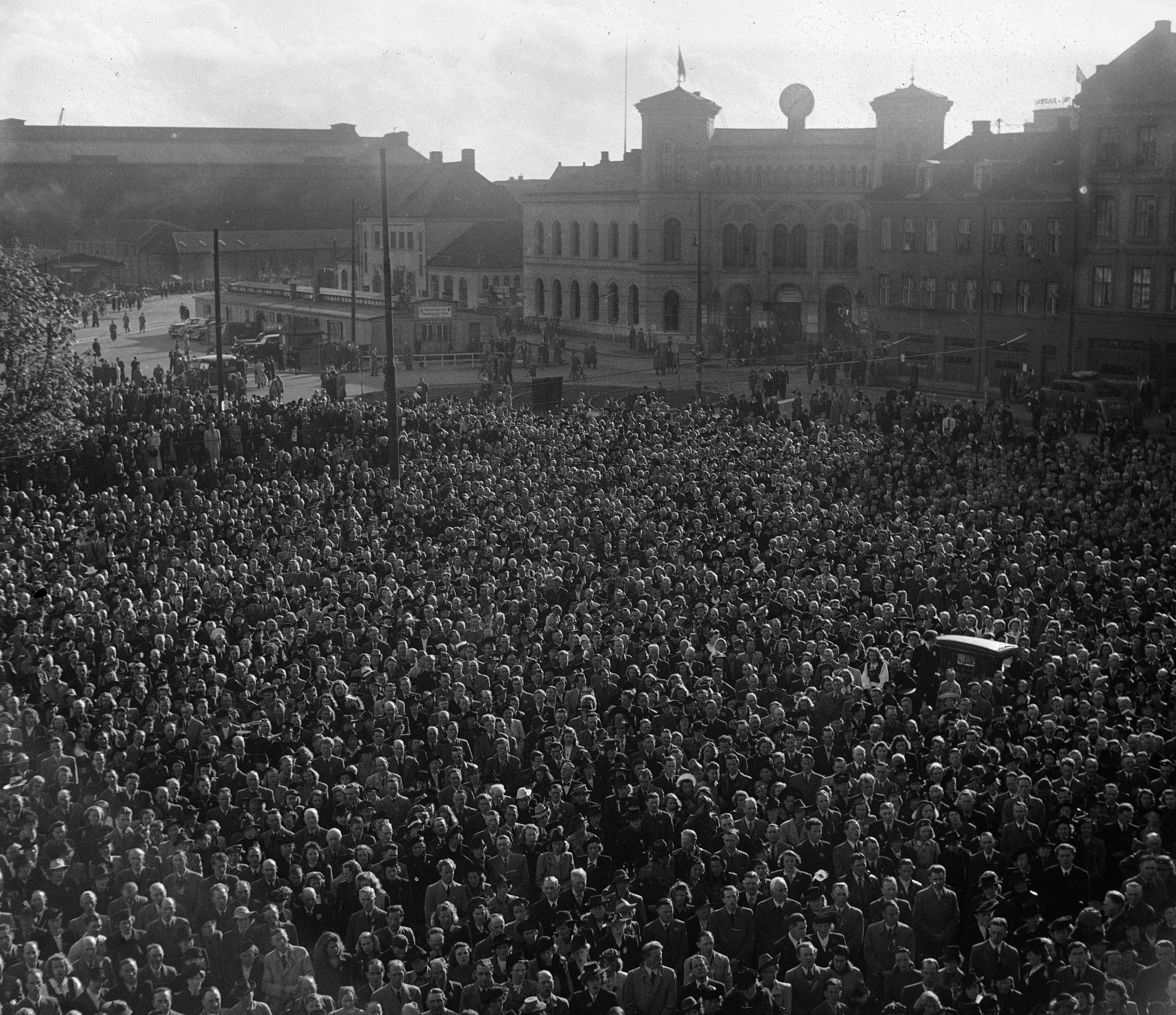 17.mai -feiring Oslo 1945. Regn la ingen demper på festlighetene under den første feiringen av nasjonaldagen etter krigen. Her folkemassen som deltok i festmøtet på Rådhusplassen. Vestbanen i bakgrunnen.