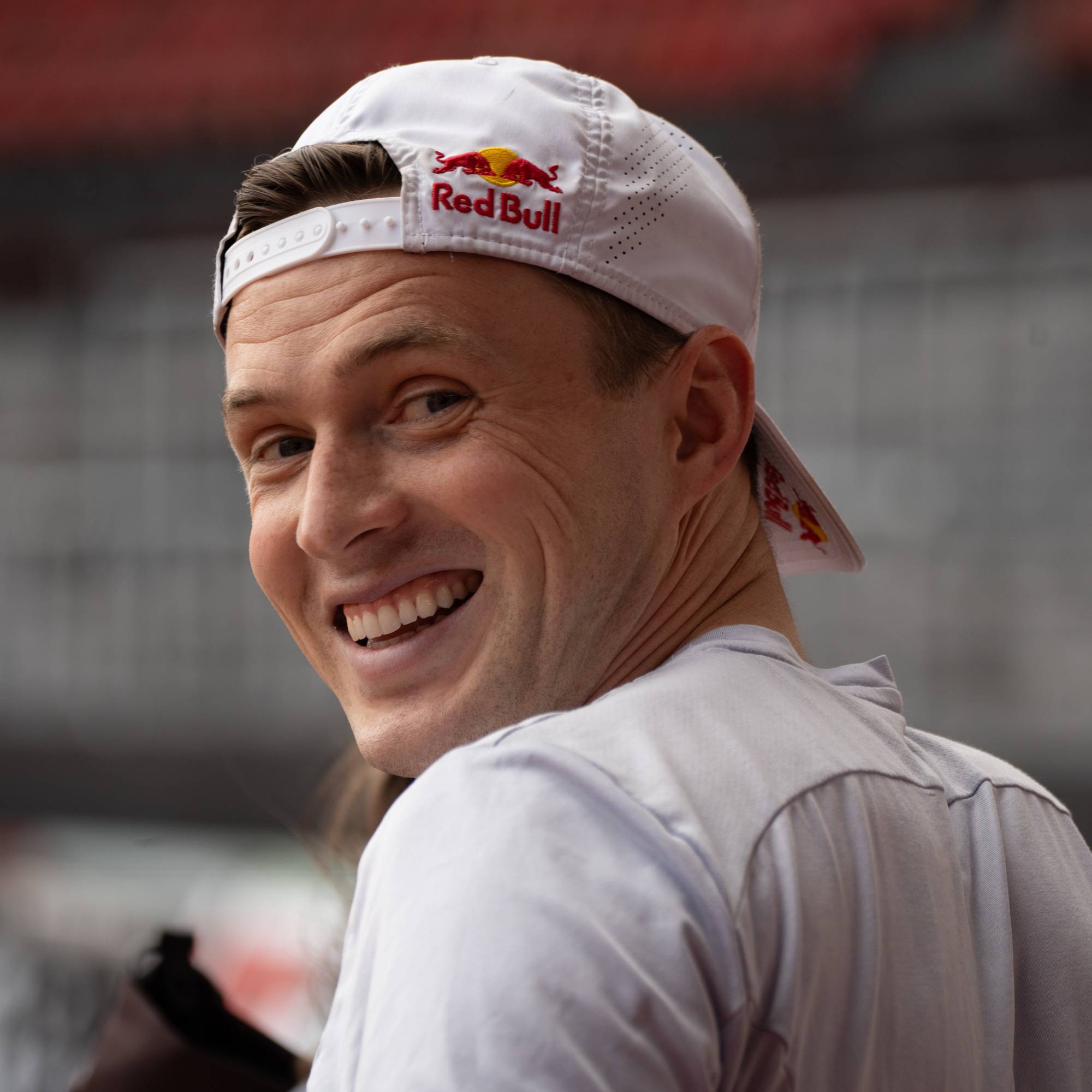 En smilende mann med hvit caps fra Red Bull ser mot kamera. Bakgrunnen er utydelig. (Bildebeskrivelsen er laget av en KI-tjeneste)