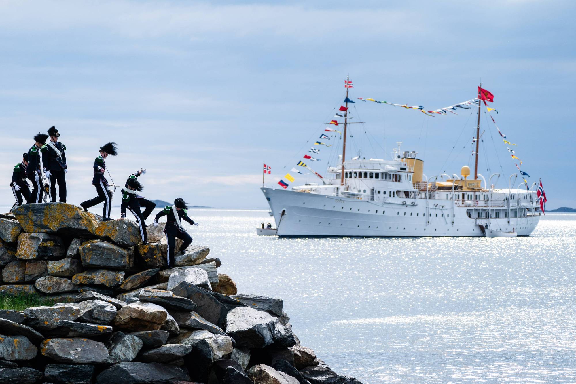 Gardister går ned fra en steinmur, i bakgrunnen ligger kongeskipet "Norge"