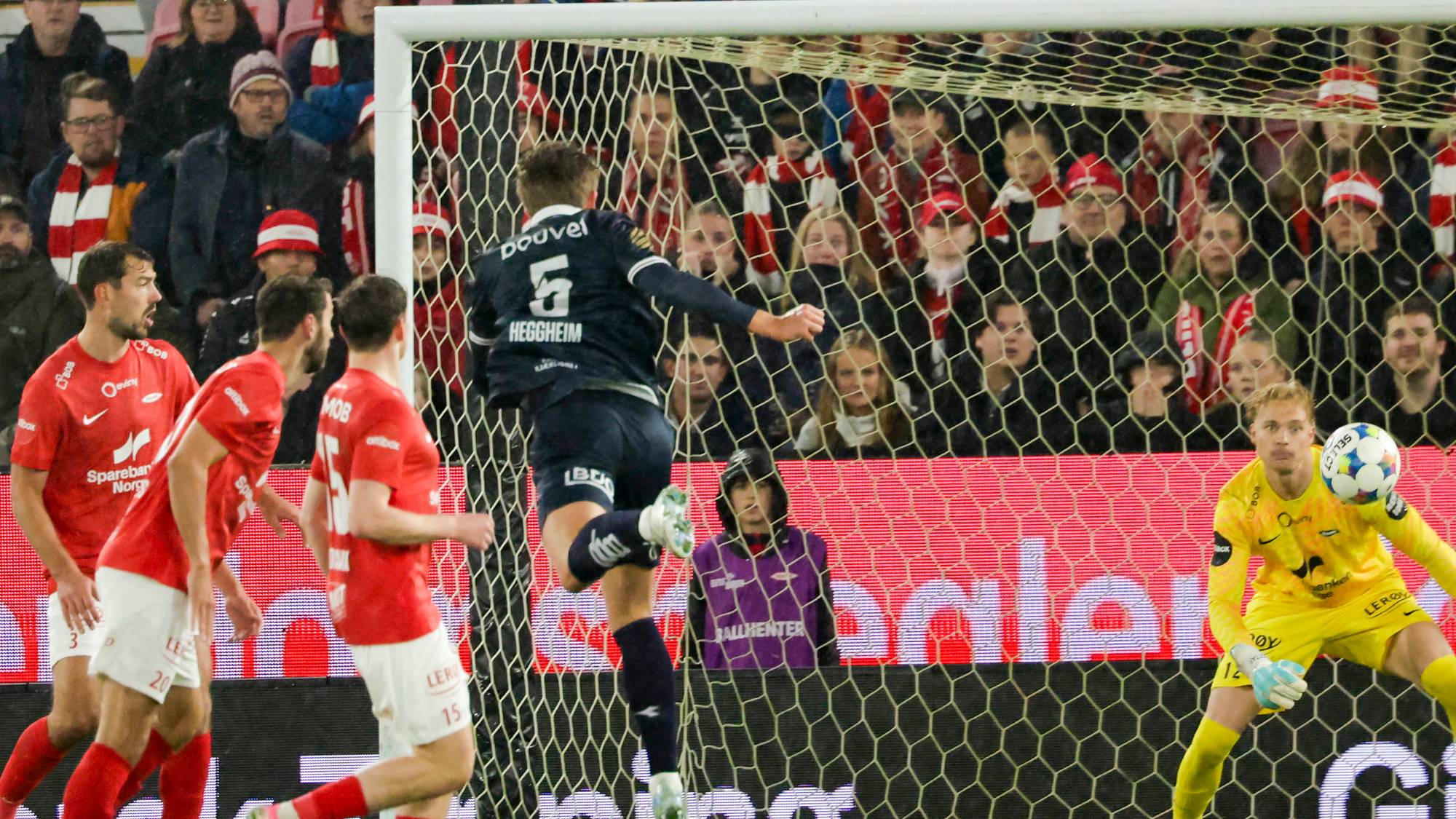 Fotballspilleren Heggheim skyter mot mål foran publikum og en keeper i gul drakt. (Bildebeskrivelsen er laget av en KI-tjeneste)
