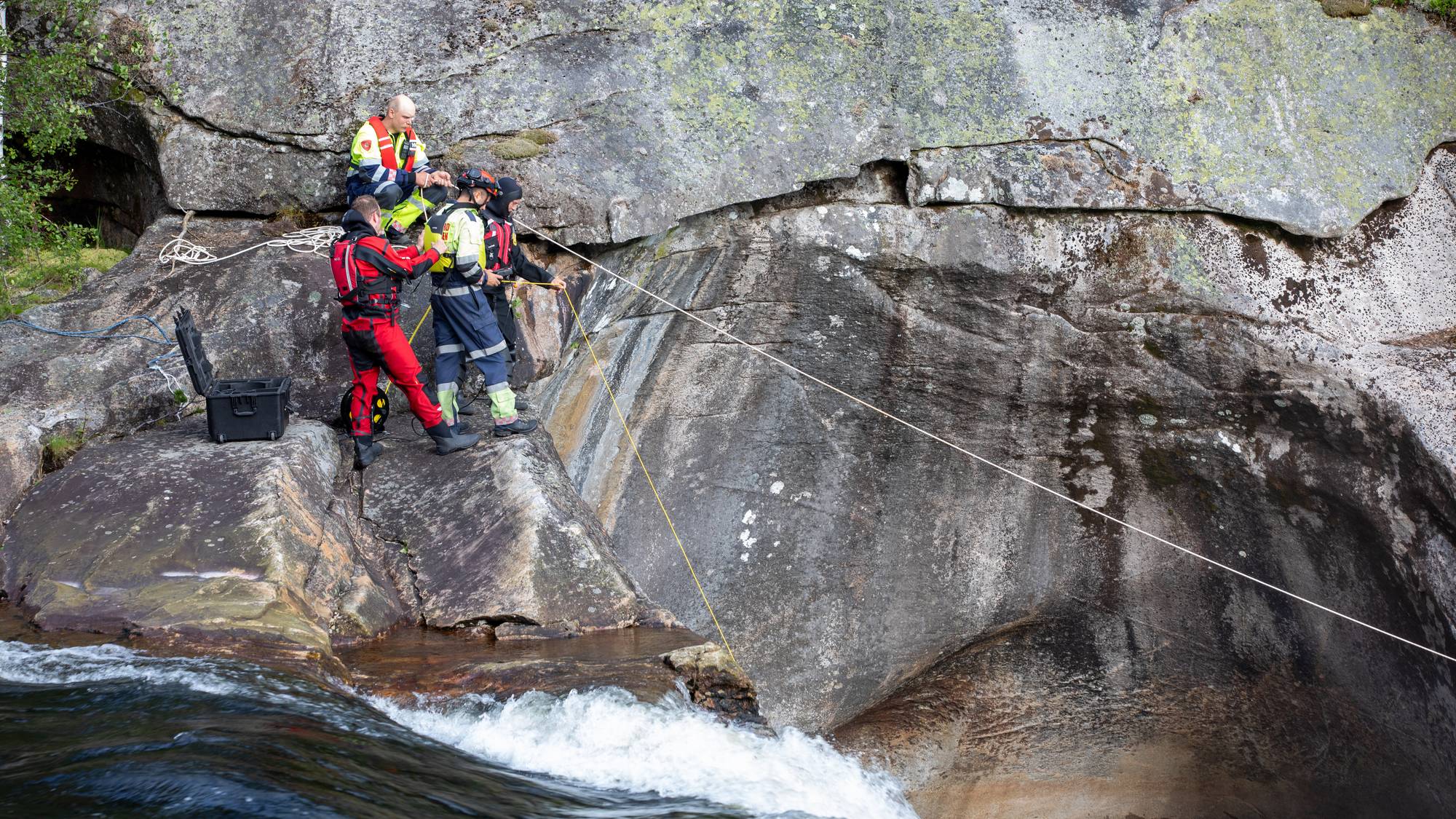 Redningsmannskaper i verneutstyr bruker tau for å sikre et område ved en foss. (Bildebeskrivelsen er laget av en KI-tjeneste)