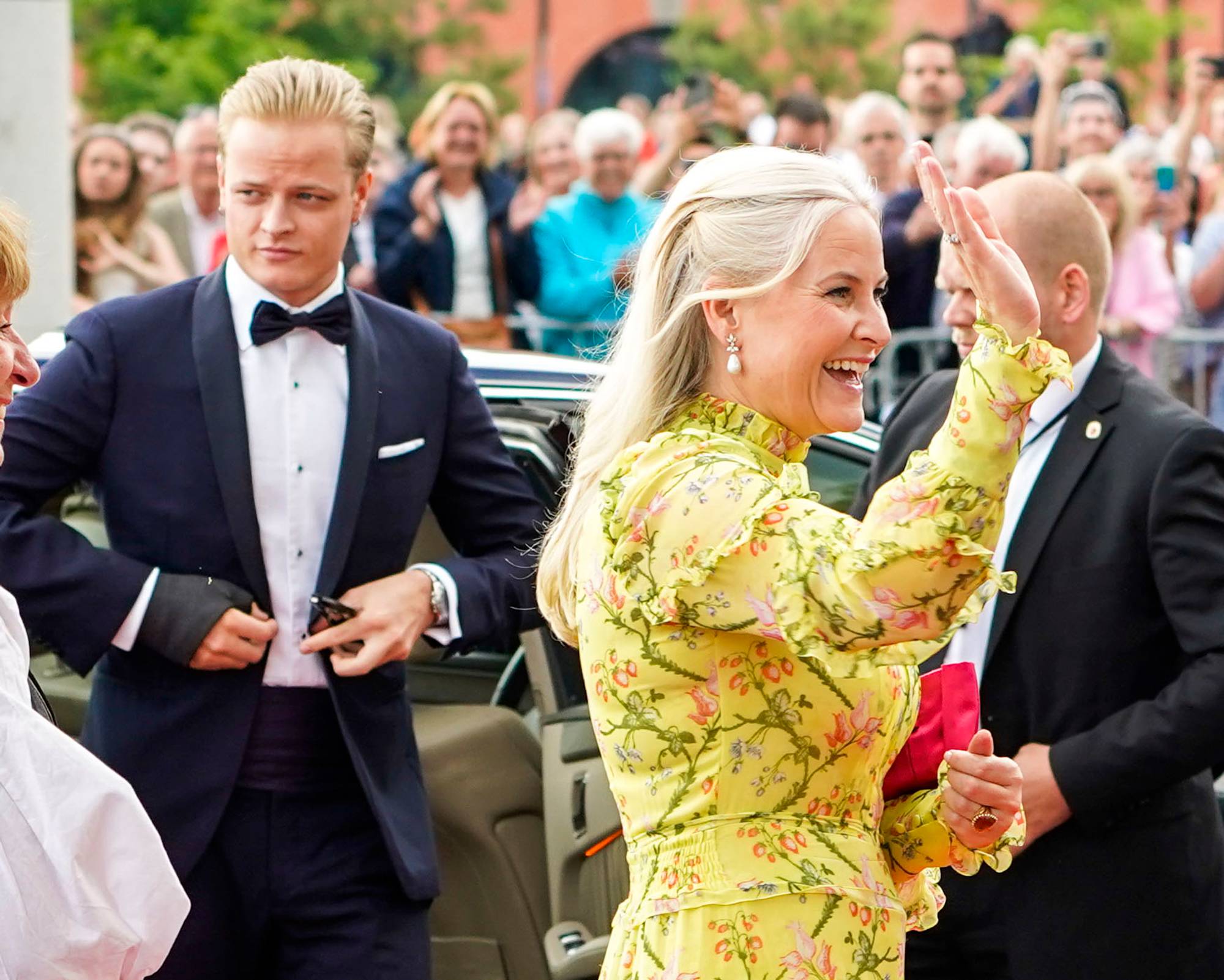Kronprinsesse Mette-Marit vinker til publikum. Marius Borg Høiby står ved siden av henne. (Bildebeskrivelsen er laget av en KI-tjeneste)