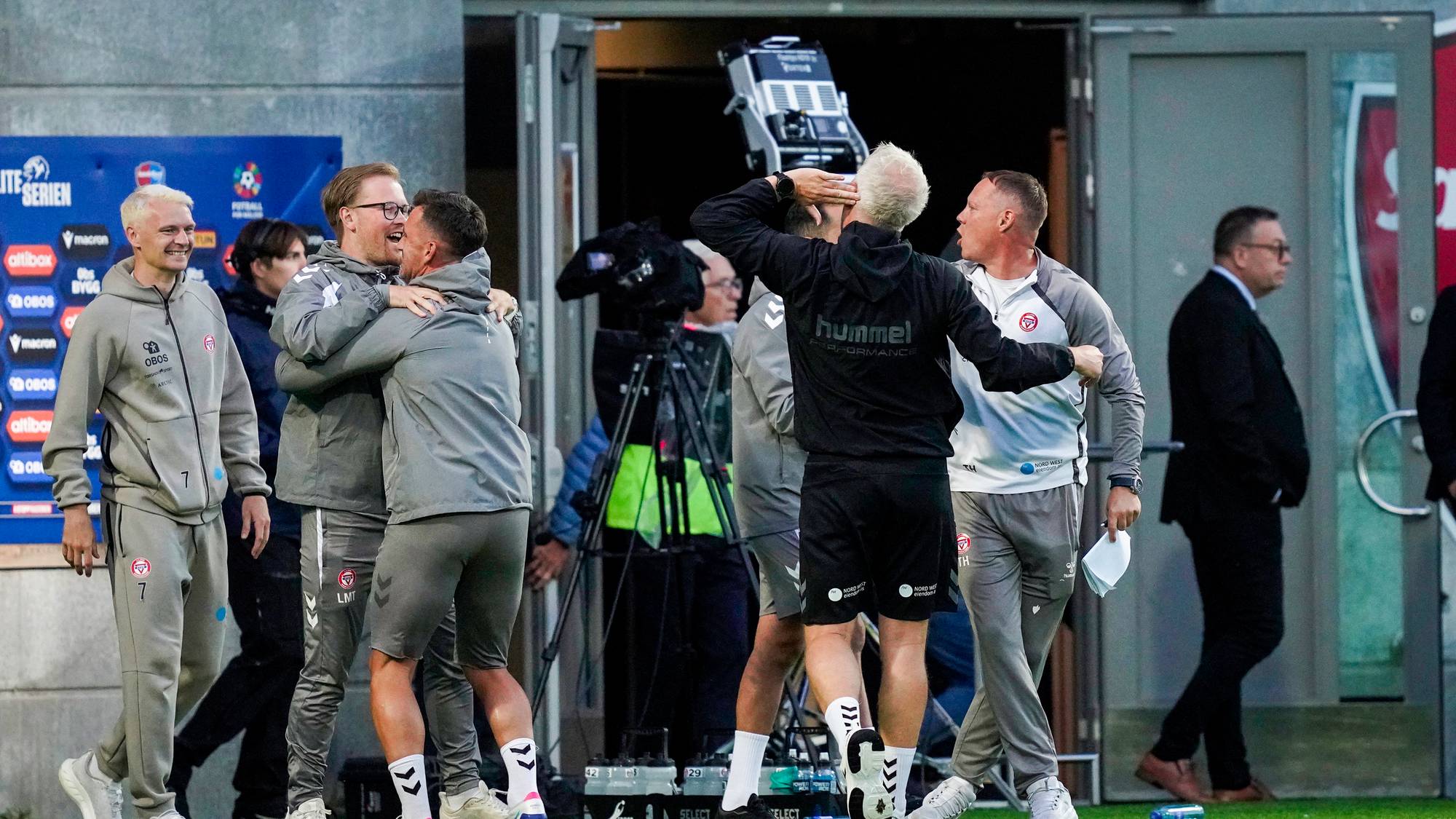 Trenere og støtteapparat i treningsklær feirer med klemmer ved spillertunnelen på en fotballstadion. (Bildebeskrivelsen er laget av en KI-tjeneste)