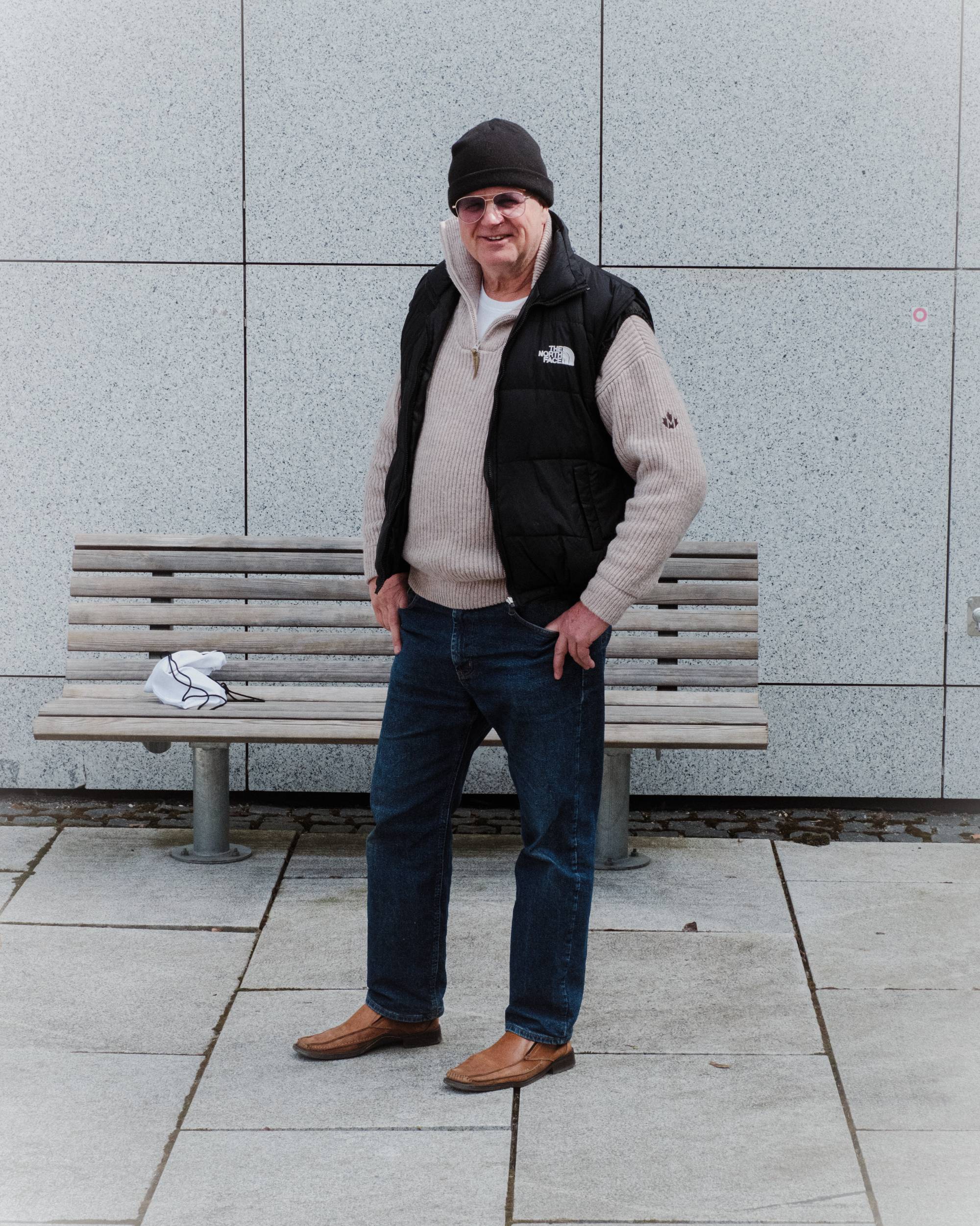En mann med jeans, North Face-vest, solbriller og lue poserer for kamera