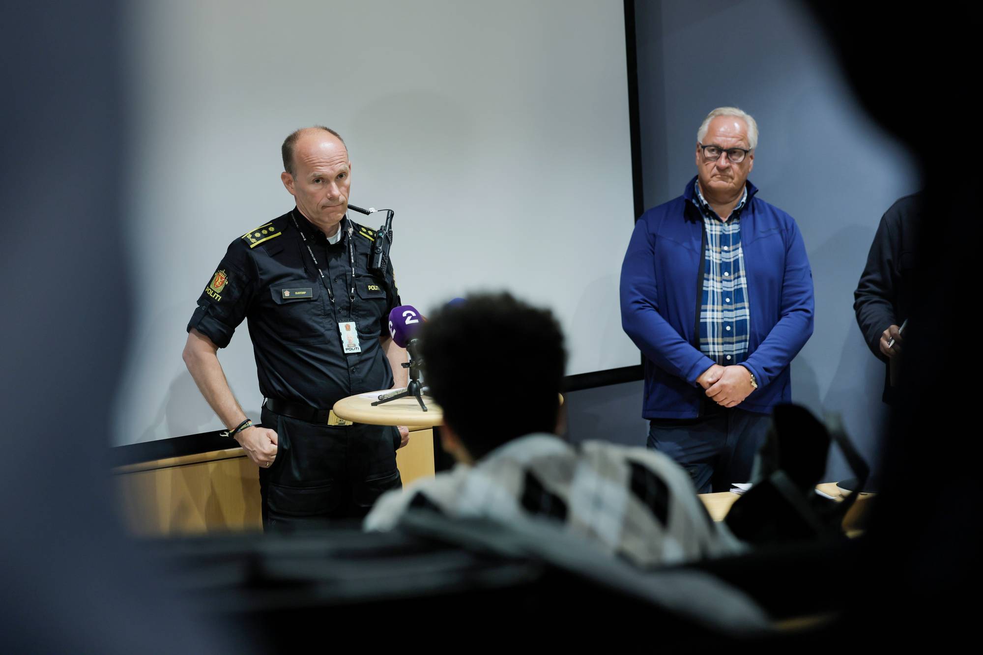 Politimann i uniform holder pressekonferanse med en mann stående ved siden av seg. 