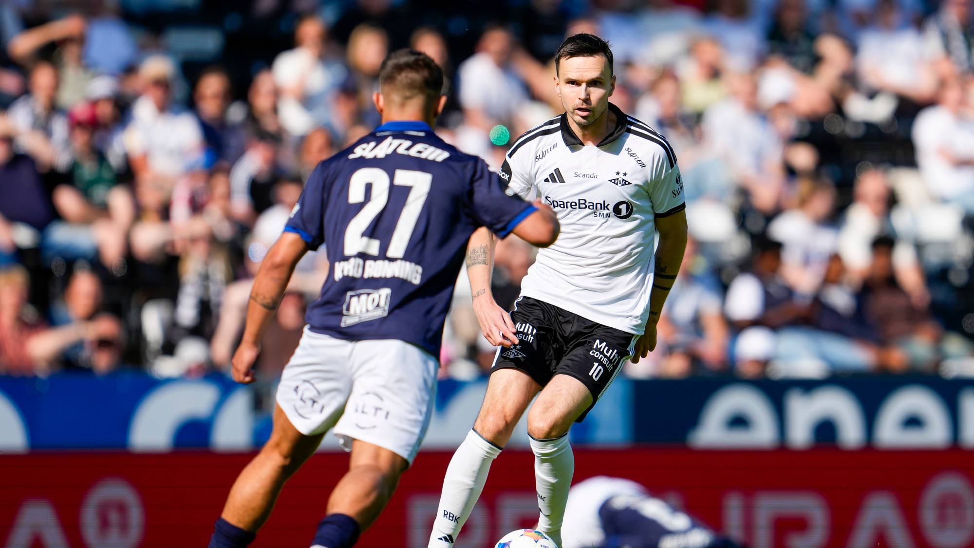 et par fotballspillere på en bane med et publikum som ser på (Bildebeskrivelsen er laget av en KI-tjeneste)