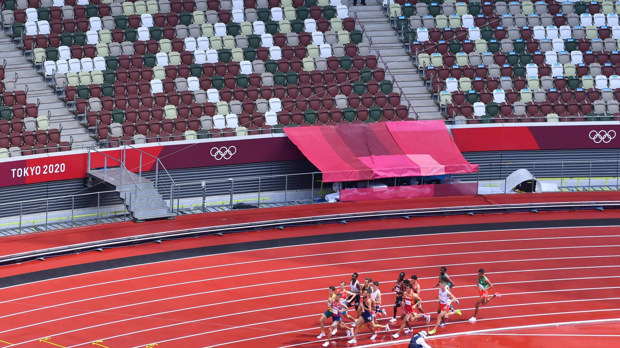 Løpere i et friidrettsløp på en rød løpebane under Tokyo 2020. Tomme tribuner i bakgrunnen. (Bildebeskrivelsen er laget av en KI-tjeneste)