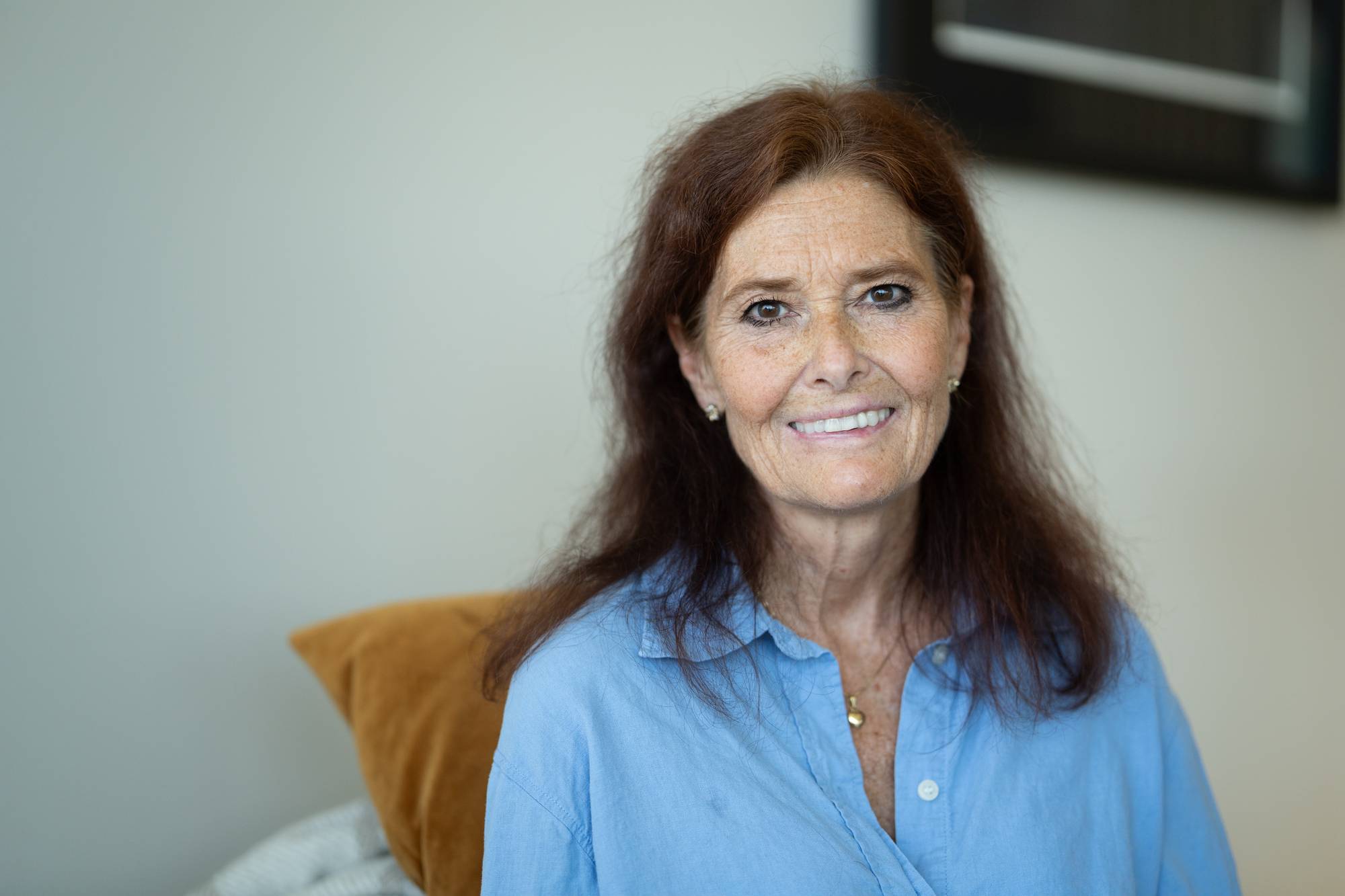 Irene Mjelde ser rett inn i kamera og smiler. Ho har raudbrunt langt hår og ei blå skjorte. 