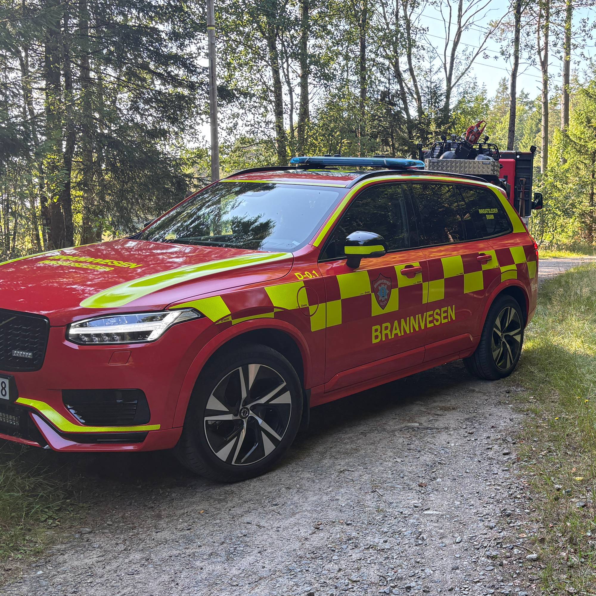 Rød bil fra brannvesenet parkert på en grusvei i et skogsområde. (Bildebeskrivelsen er laget av en KI-tjeneste)